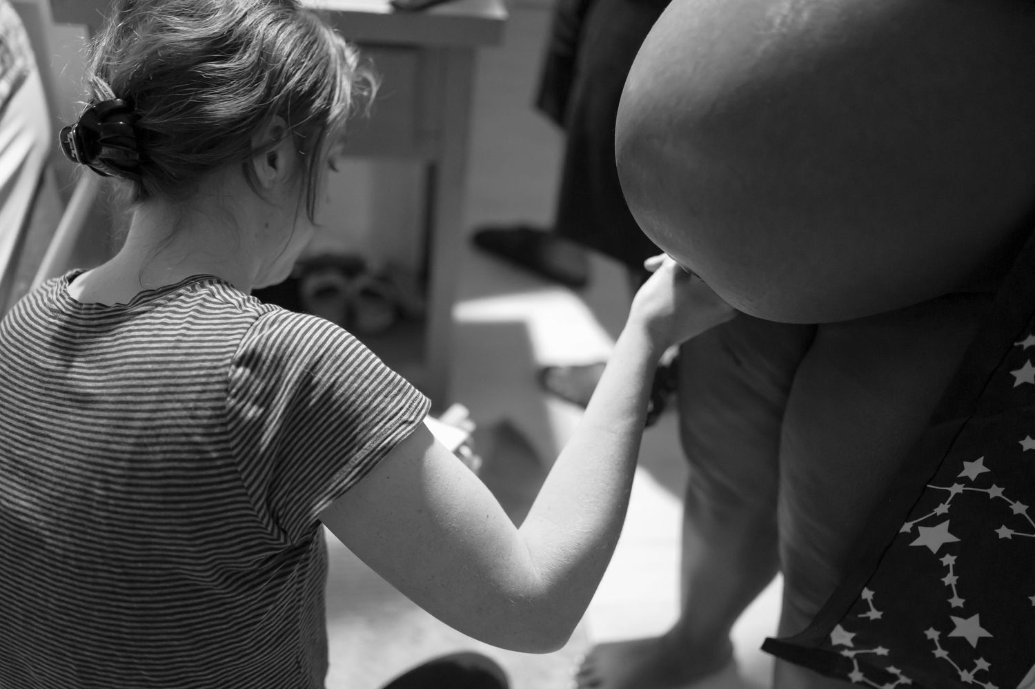 Black and white photo showing hands supporting a pregnant belly during labor.