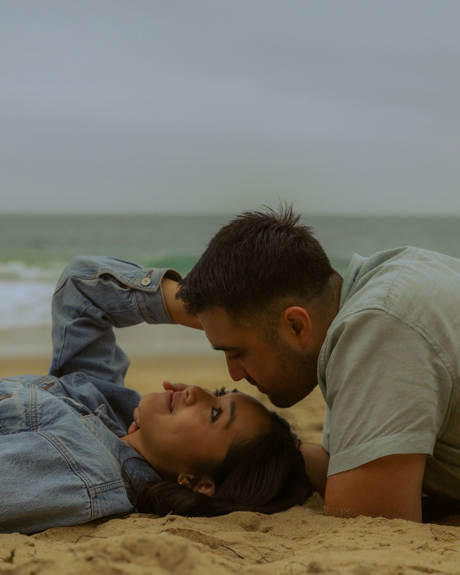 Romantic couple lying together on sandy beach during overcast day.