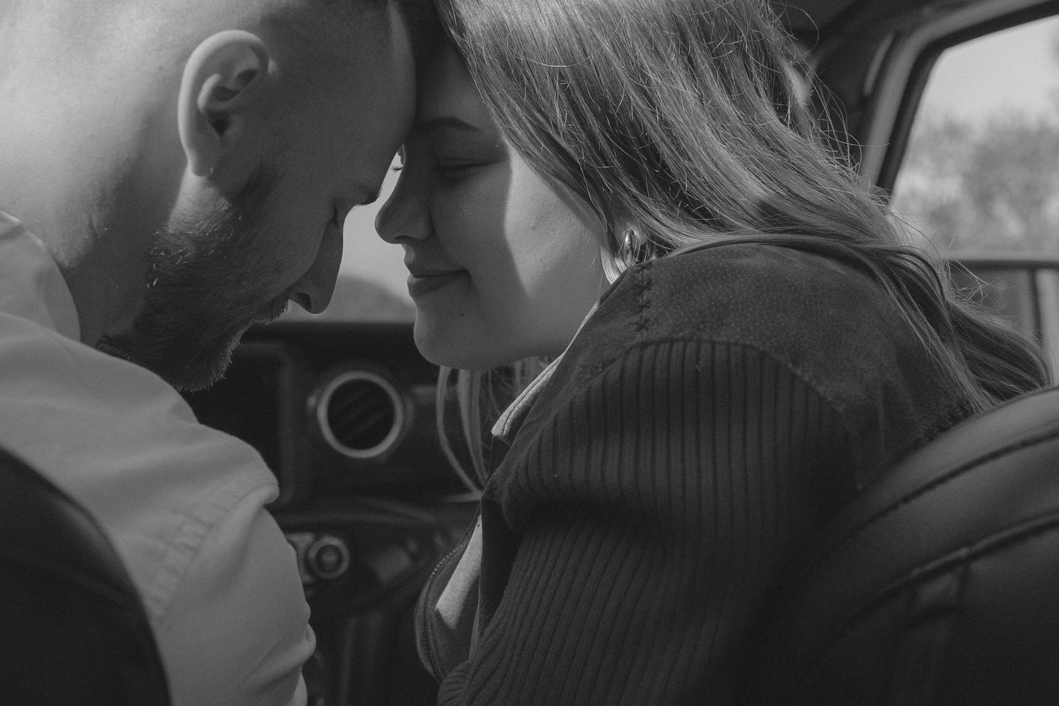 Monochrome portrait of couple sharing an intimate moment inside car interior.