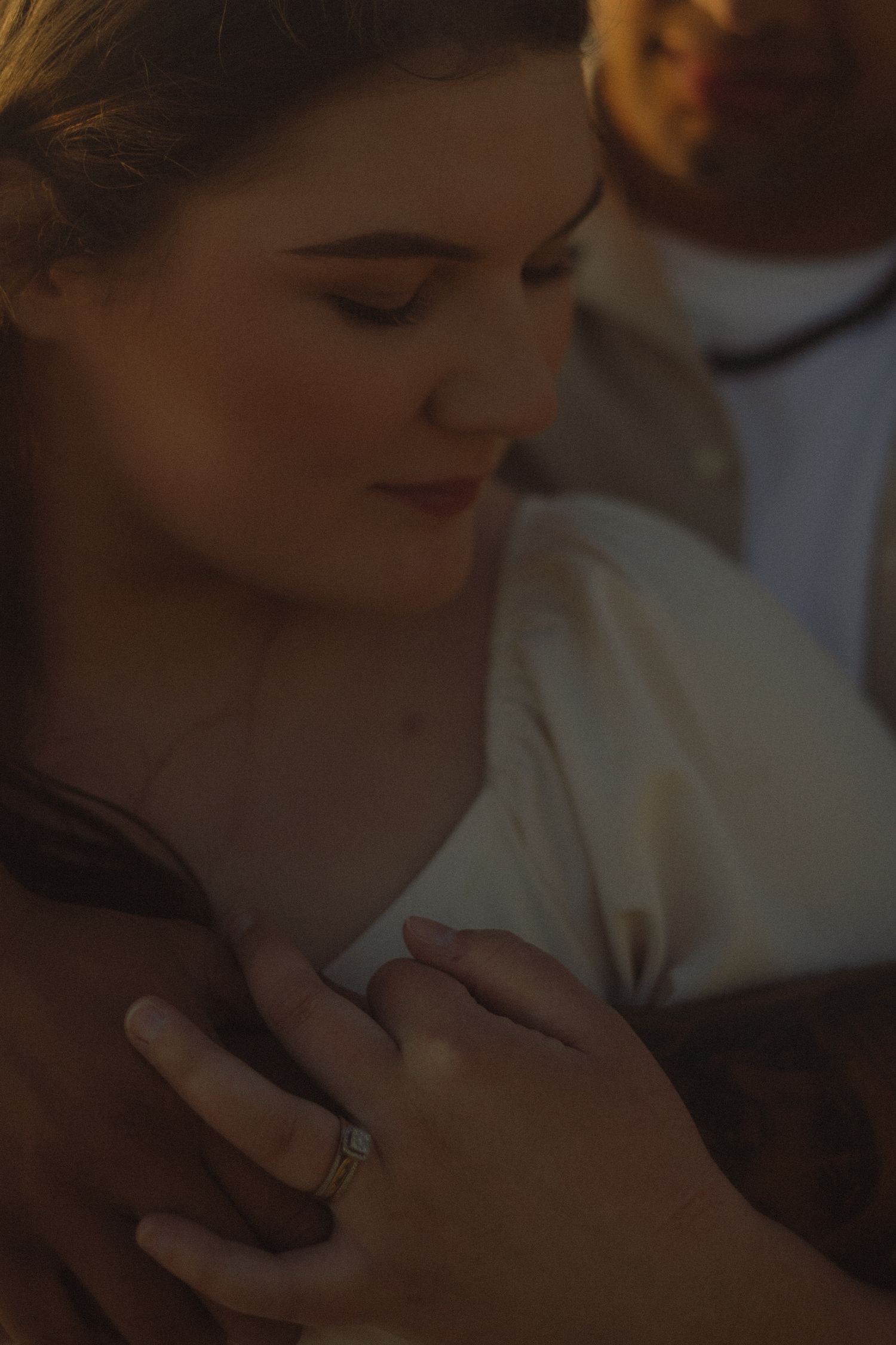 Close-up shot of a hand wearing an engagement ring in warm atmospheric lighting.