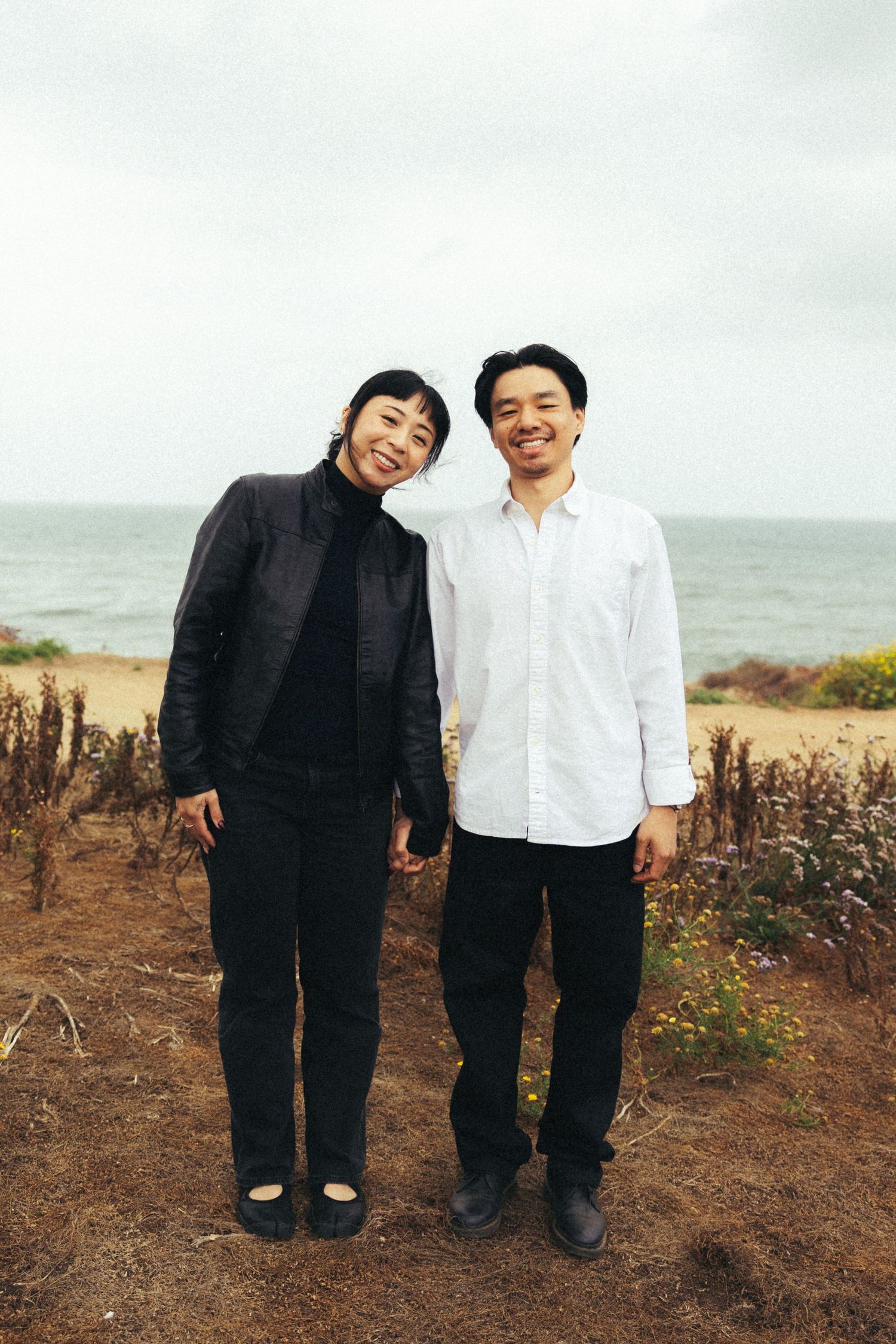 Two smiling people standing together on a coastal bluff with ocean views on an overcast day.