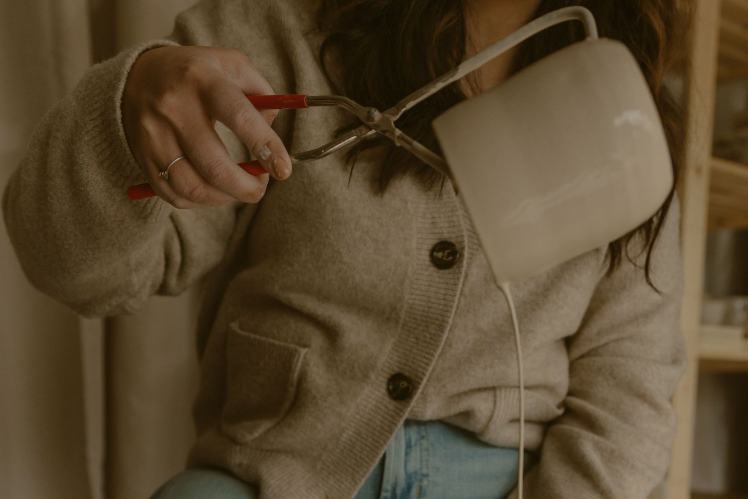 Person in beige cardigan holding pottery tools in a studio.