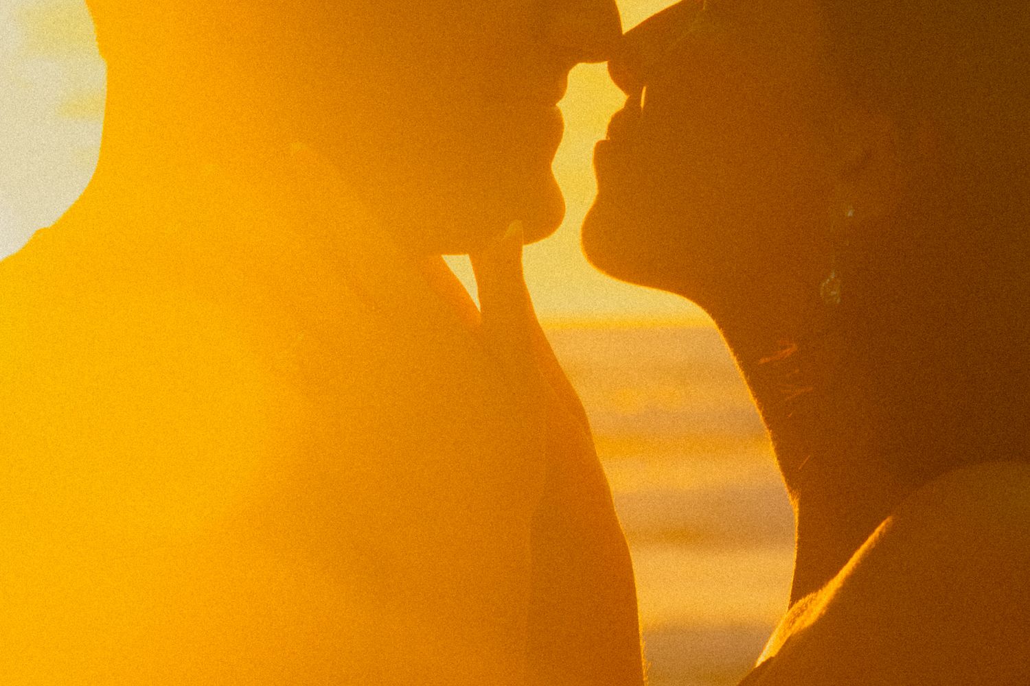 Silhouetted figures stand against a vibrant orange sunset sky creating a dramatic panoramic view.