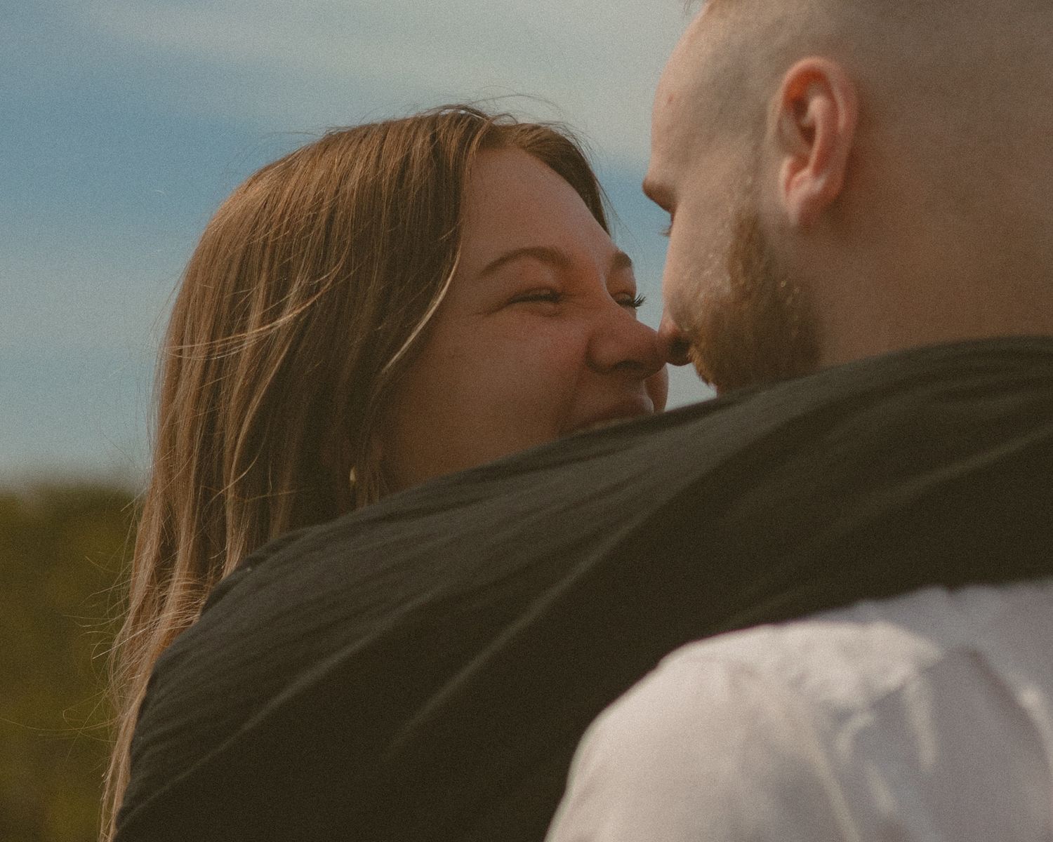 Close-up shot of couple sharing a tender moment against natural outdoor backdrop.