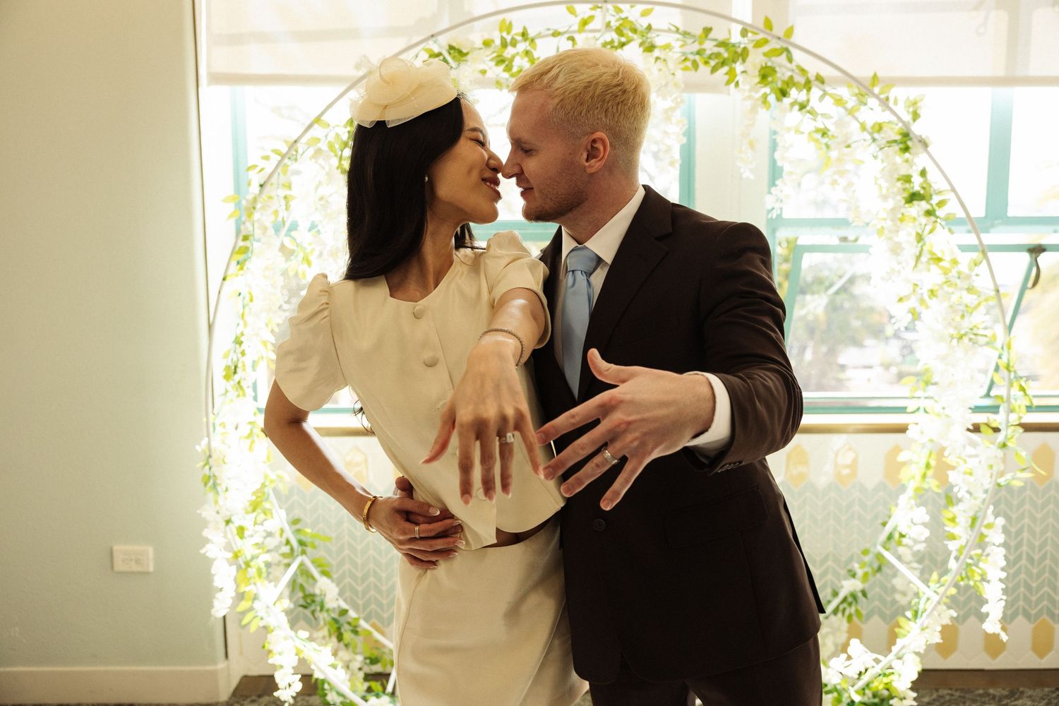 Bride and groom share a romantic moment in front of a circular floral arch at their wedding ceremony.
