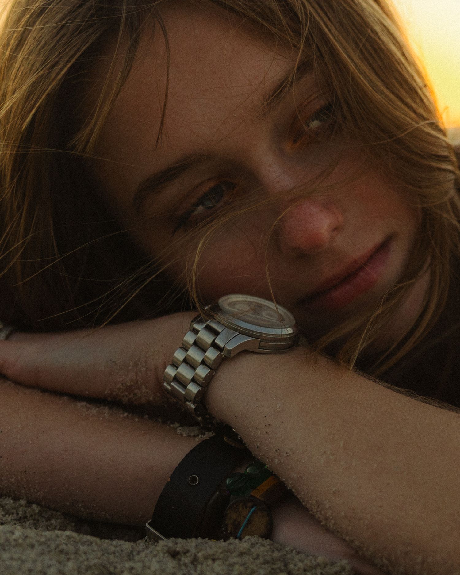 A person rests their head on their arm while wearing a watch in a dimly lit setting.