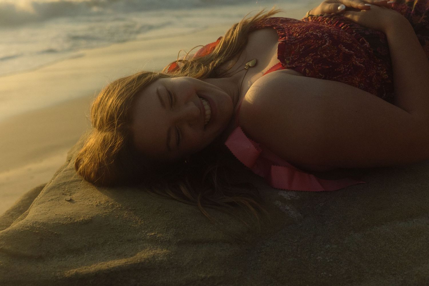 A person lies on the beach at sunset with waves gently washing over them creating a dreamy atmospheric scene.
