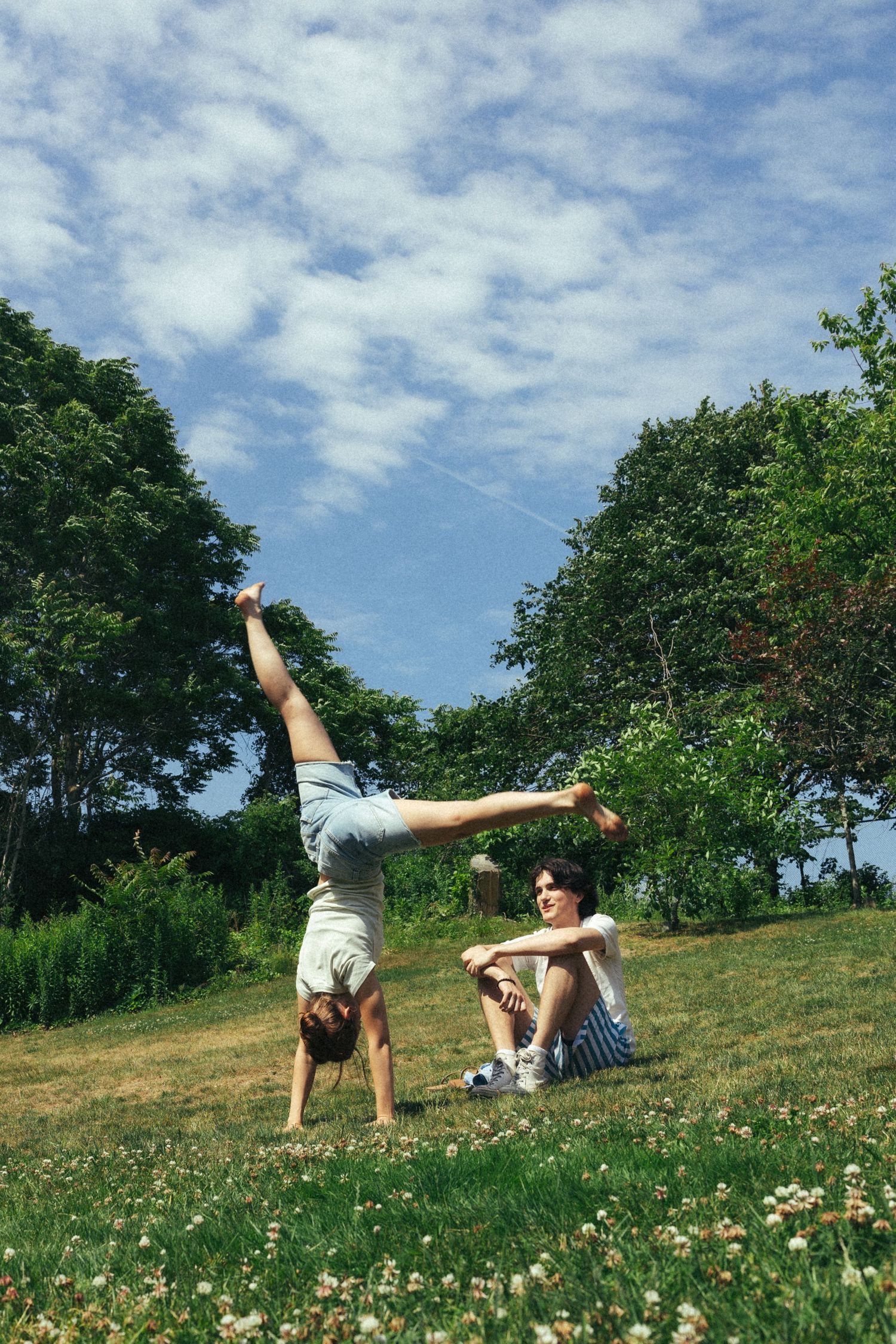 Two young women enjoying a sunny day in a park, one doing a handstand while the other sits on the grass.