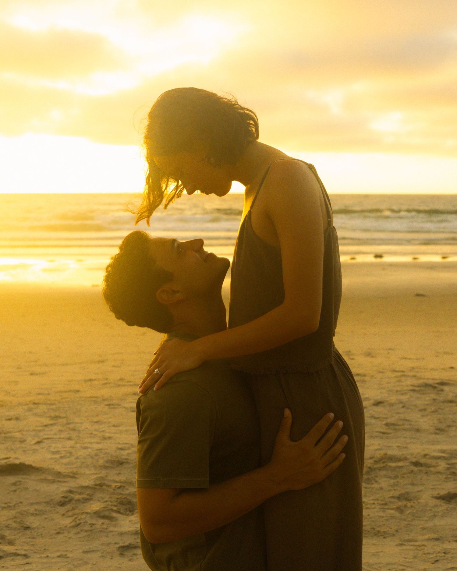 Silhouetted figures share an intimate moment on a beach during golden hour sunset.