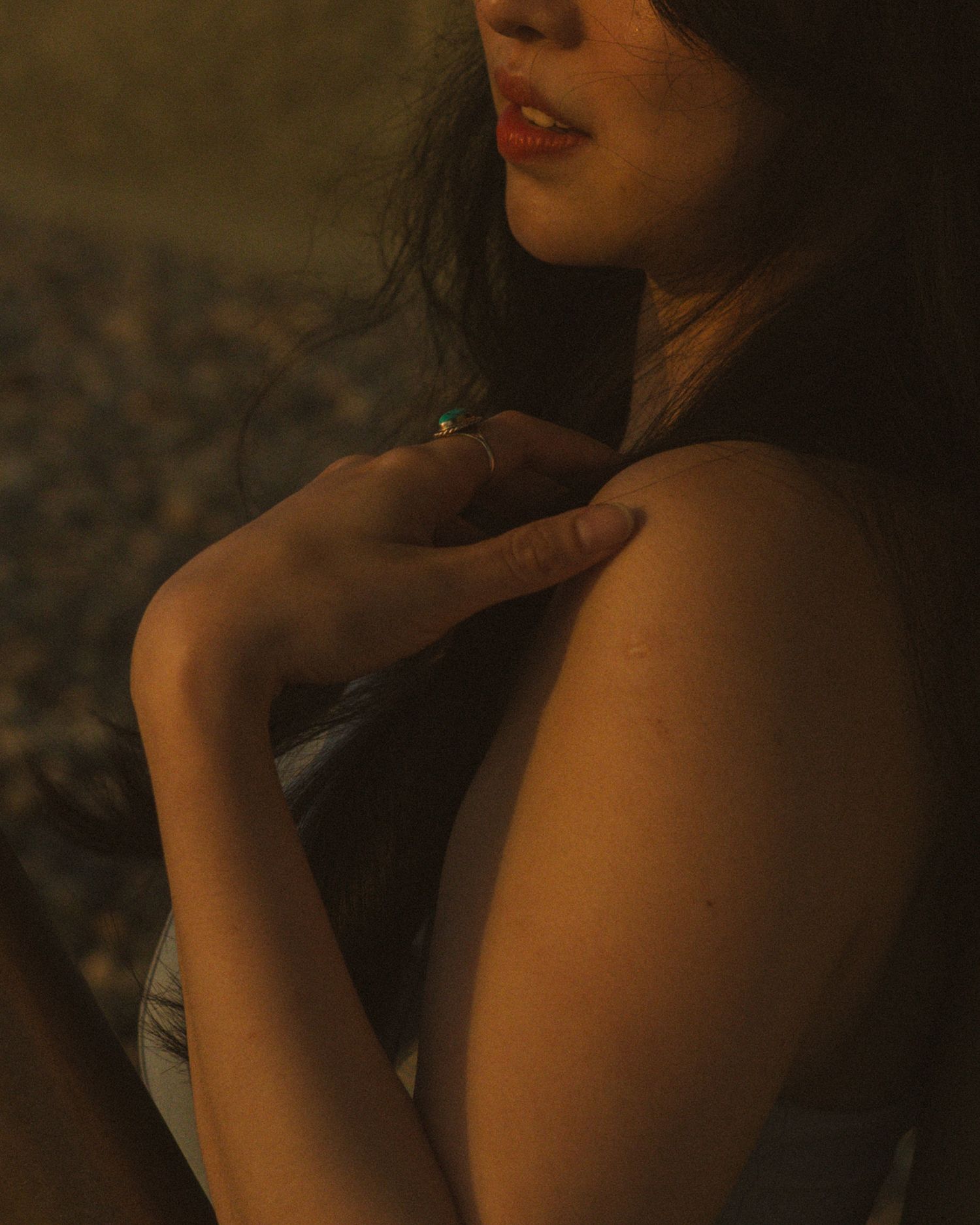 Close up portrait of someone in soft golden lighting with long dark hair against a rocky background.