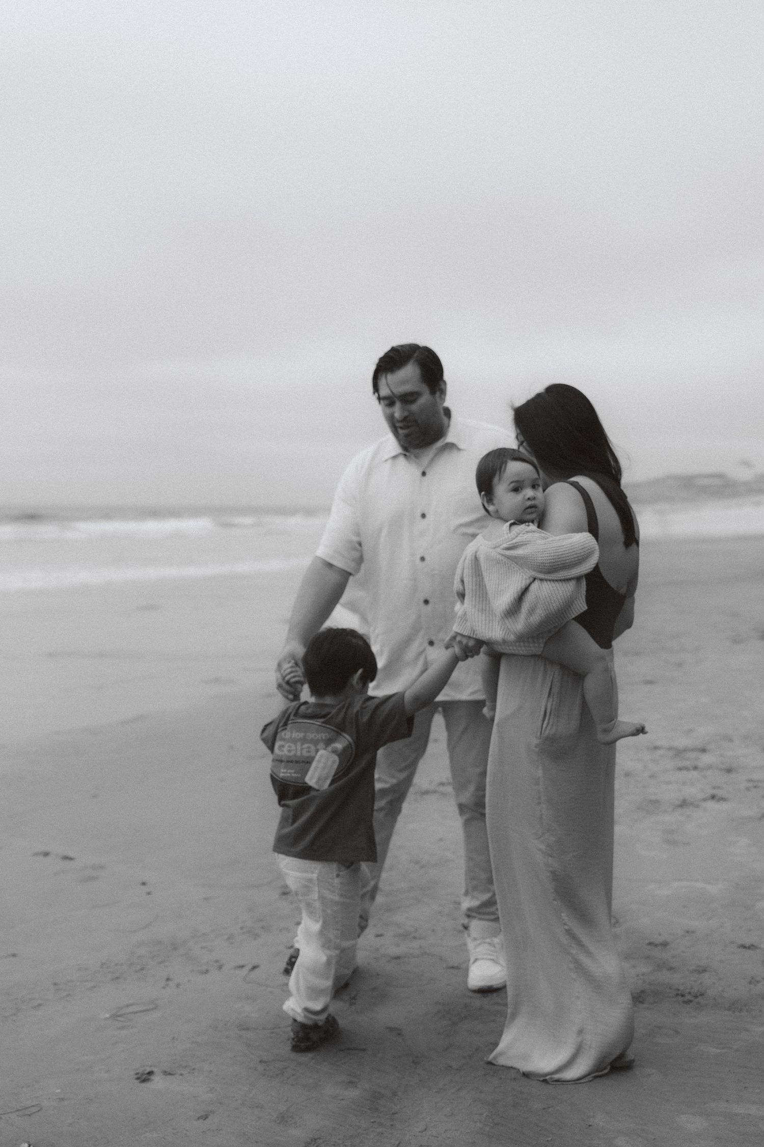 A family enjoying a quiet walk together on a misty beach shoreline in black and white.