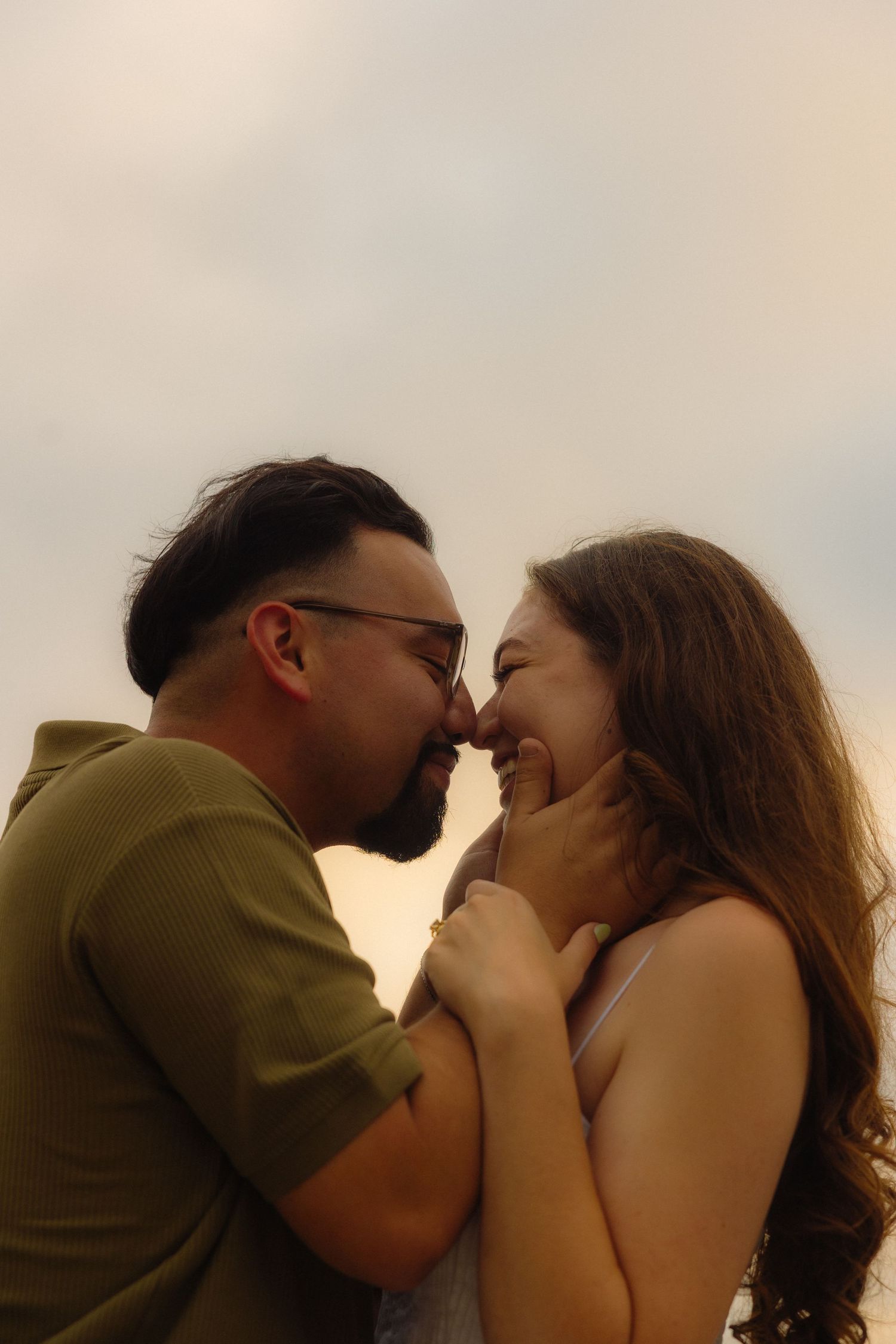 A romantic couple shares an intimate kiss at sunset against a warm sky backdrop.