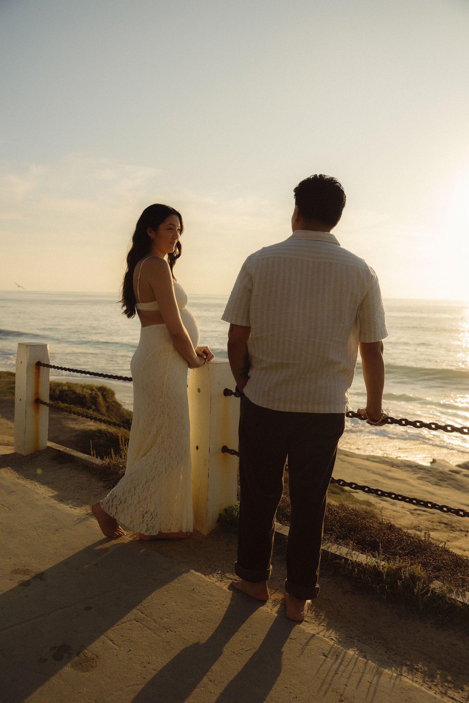 A couple walks along a coastal path at sunset, silhouetted against the golden ocean view.