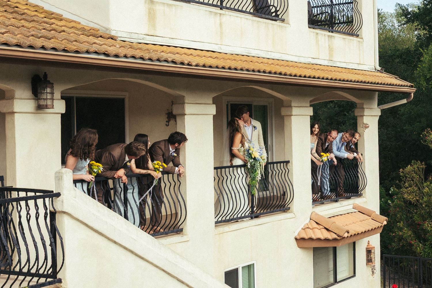 Wedding party gathered on a Spanish-style villa balcony with bride holding bouquet of sunflowers.