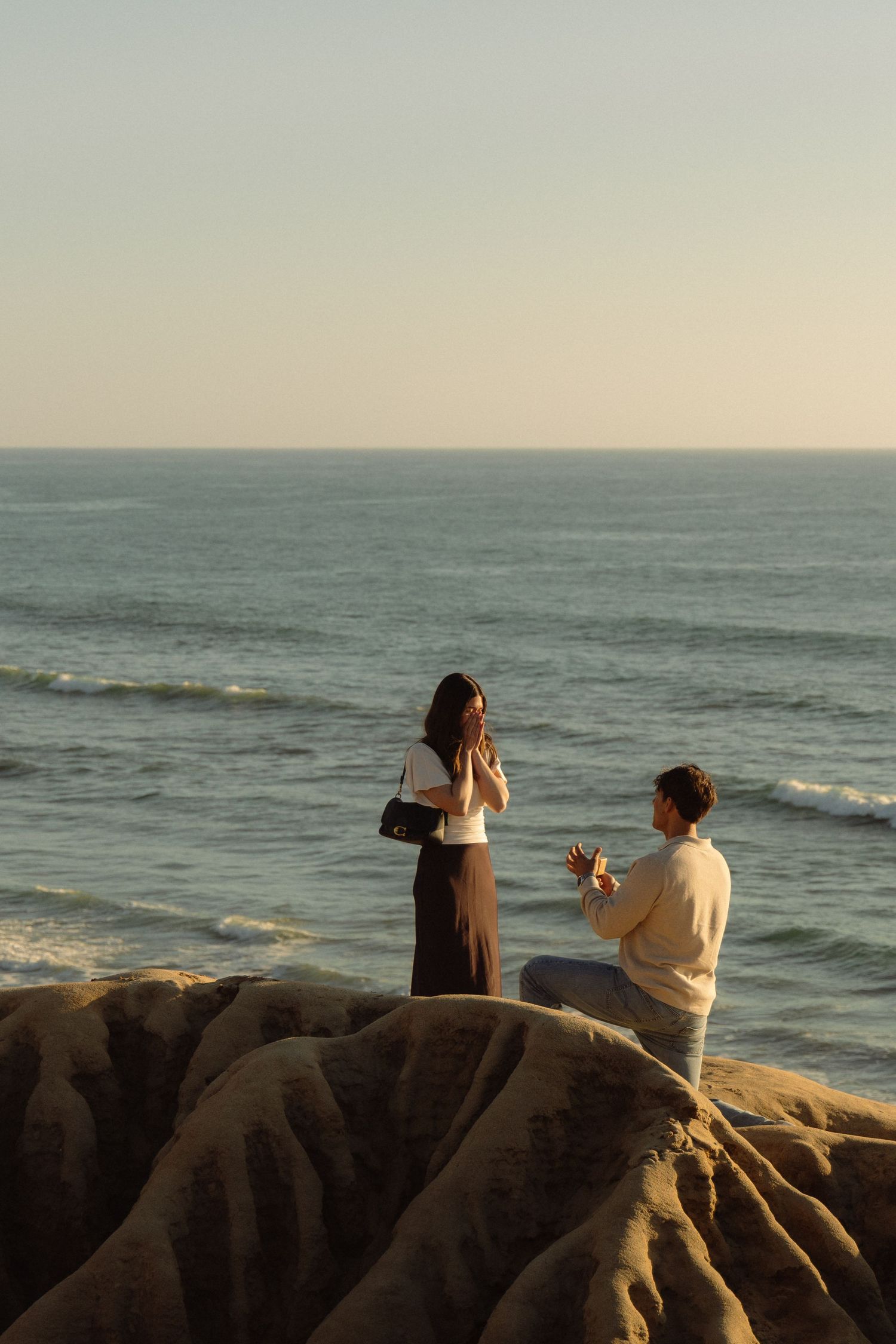 People standing on rocky cliffs overlooking the ocean at sunset while taking photos.