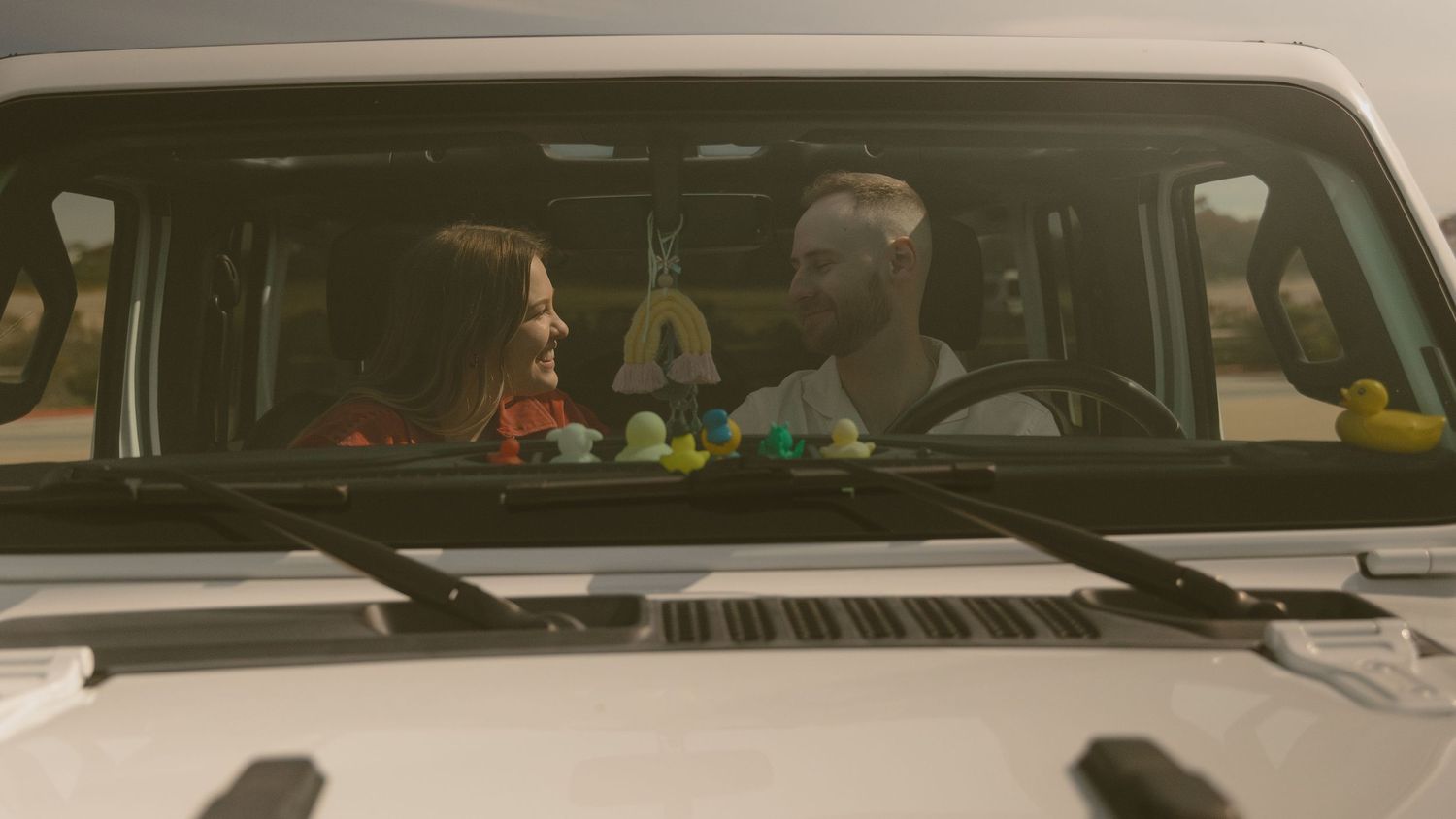 People seated in a car interior viewed through the windshield during golden hour.