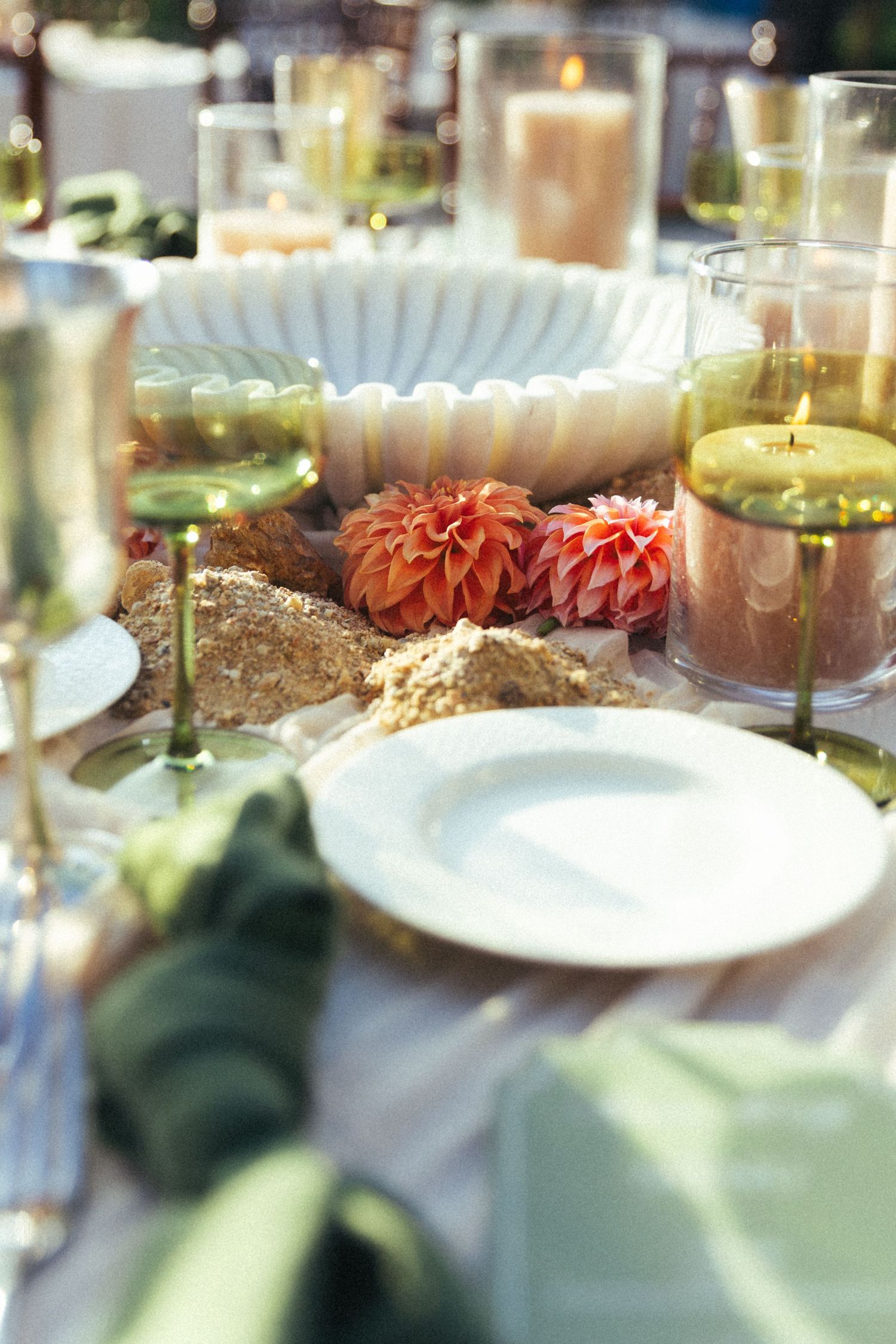 Elegant table setting with orange dahlias, lit candles, white plates, and green napkins for a sophisticated event.