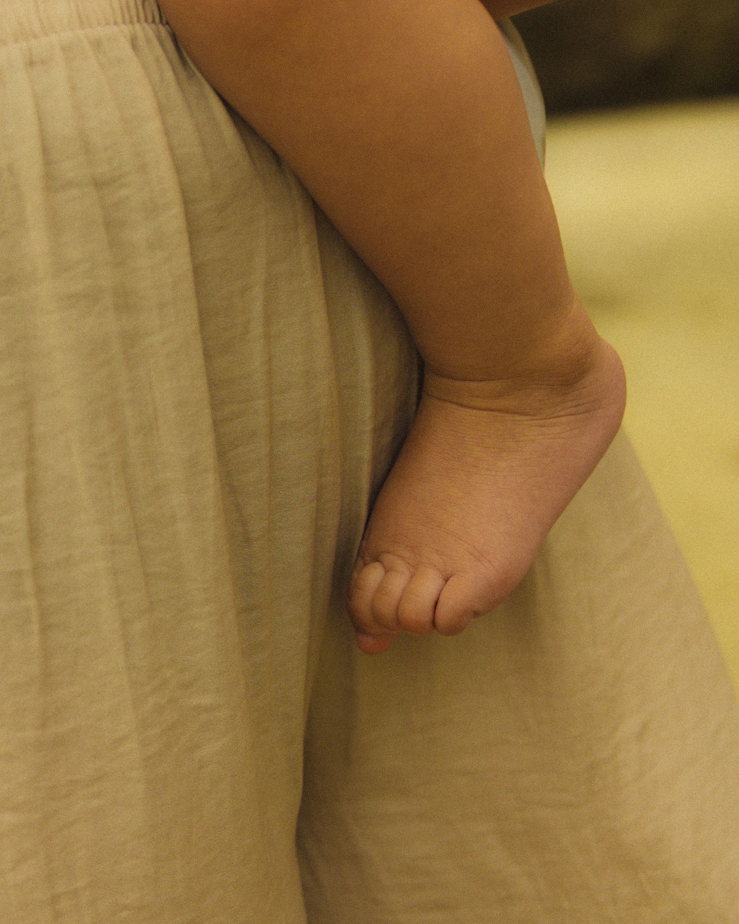 Close-up view of a tiny baby foot with chubby toes against a soft beige background.