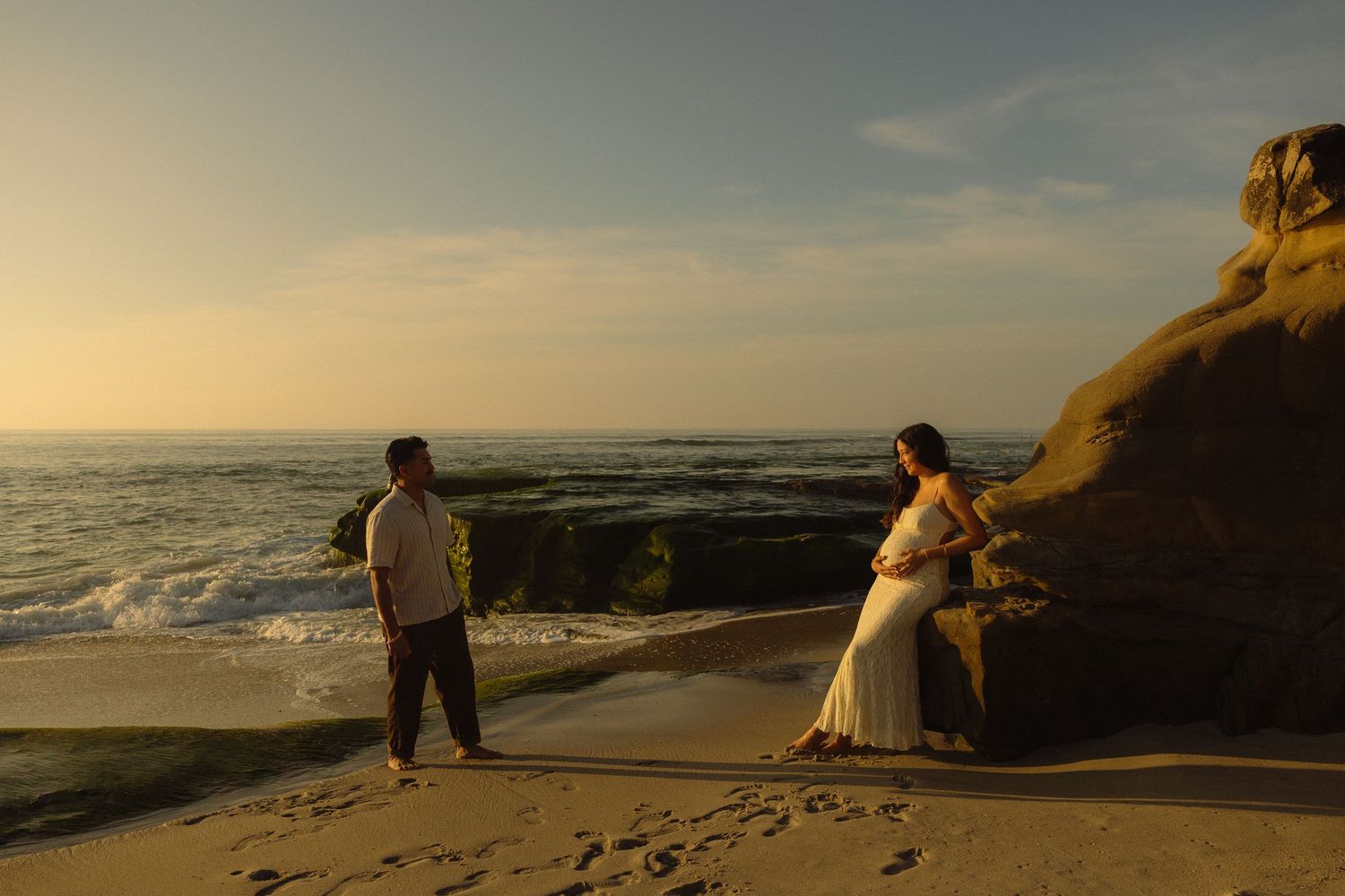 A scenic sunset panorama of a beach with cliffs and silhouetted figures enjoying the coastal view.