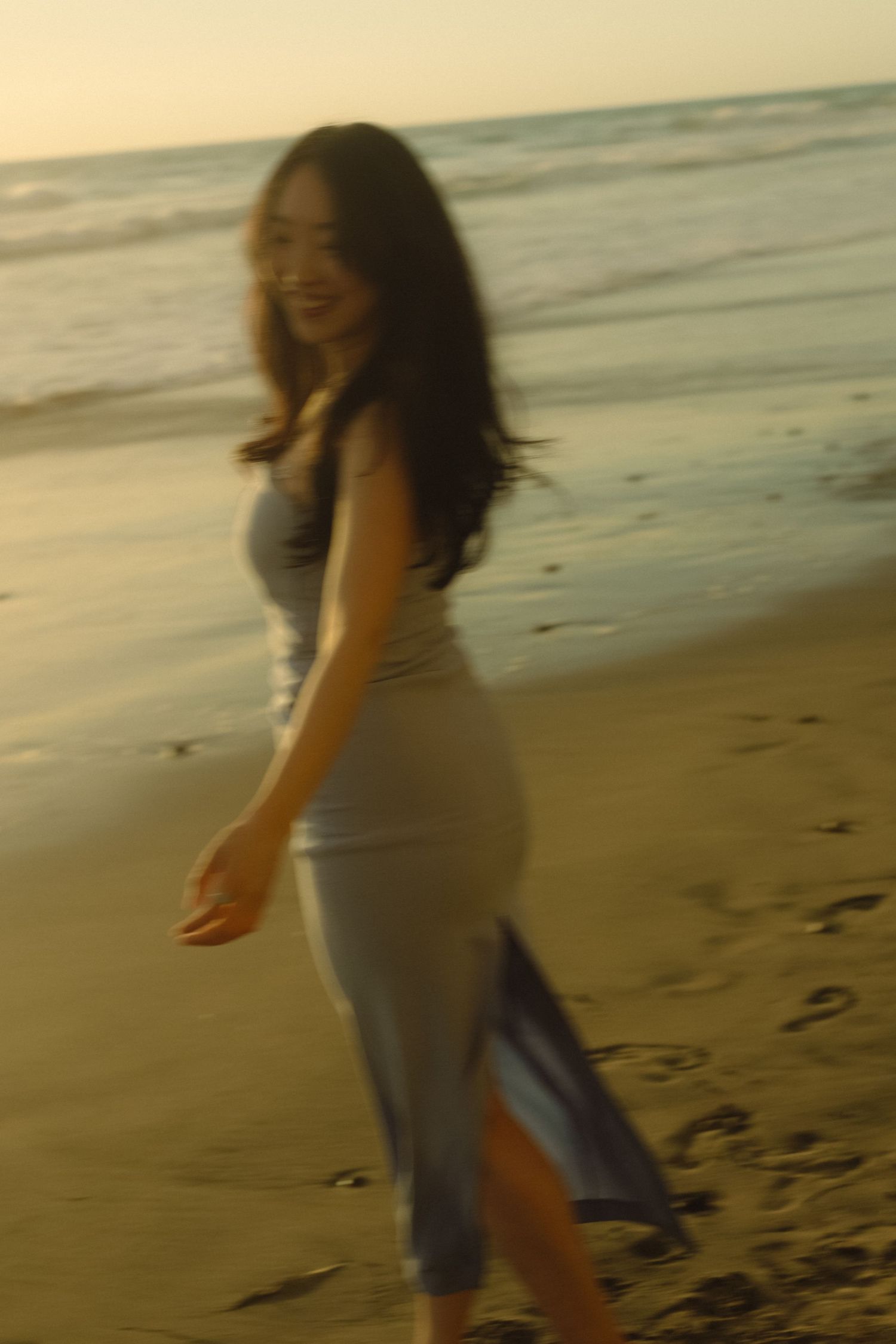 A dreamy beach scene at sunset captures a figure in a flowing dress twirling on the sandy shore.