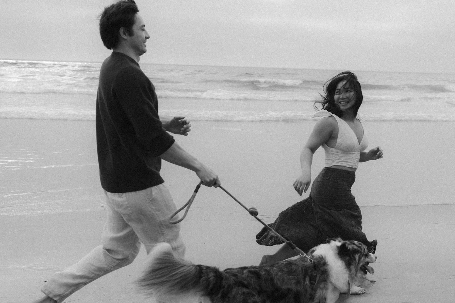 Two people engaging in playful combat moves at the beach in black and white photography.