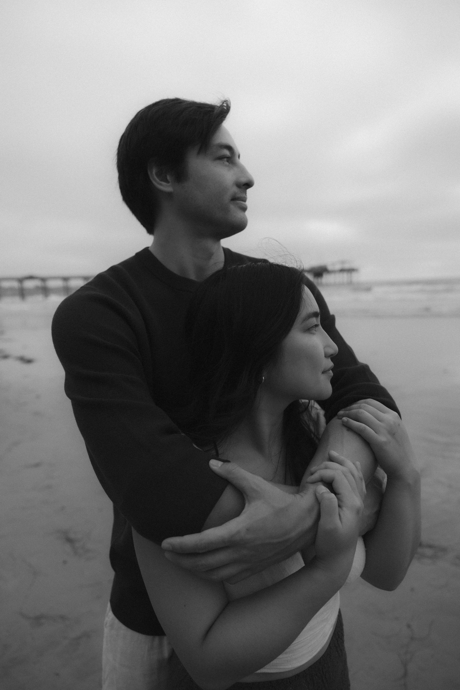 A couple embraces on a beach in black and white as they share a tender moment together.