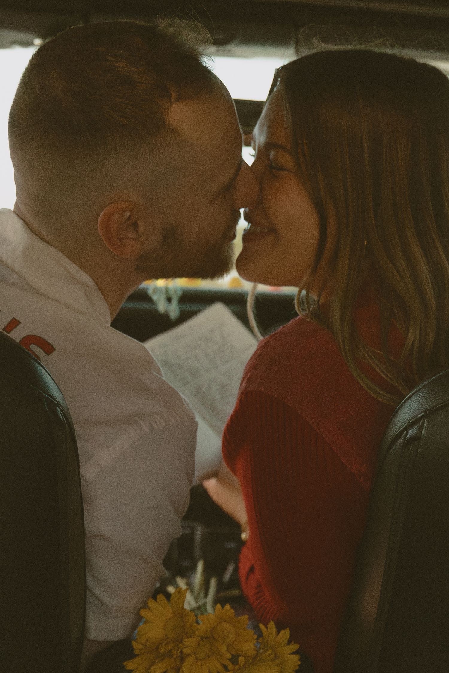 Intimate close-up of romantic couple sharing a tender moment in a car with sunlit yellow flowers.