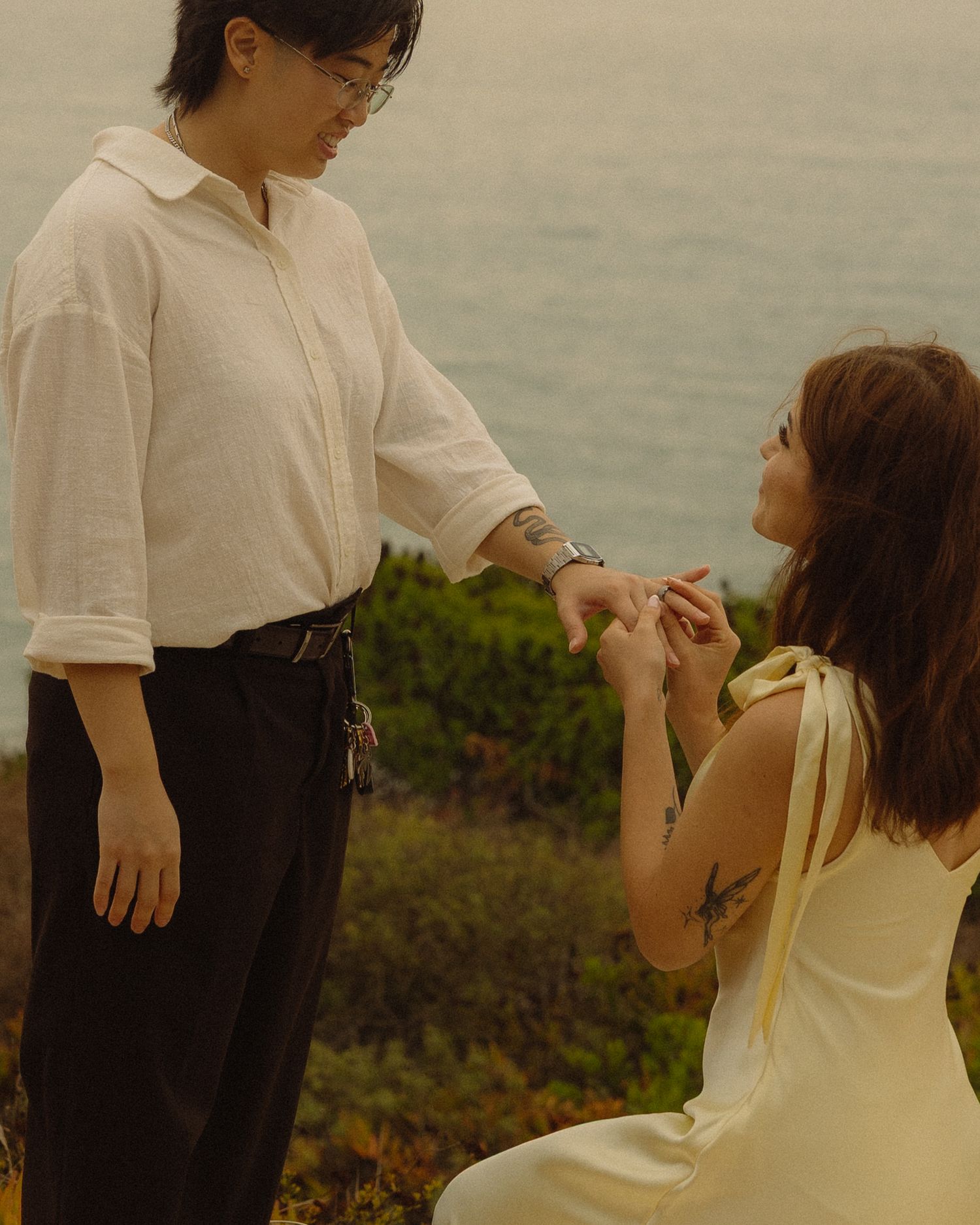 Two people in casual attire share a tender moment outdoors against a soft, natural backdrop.