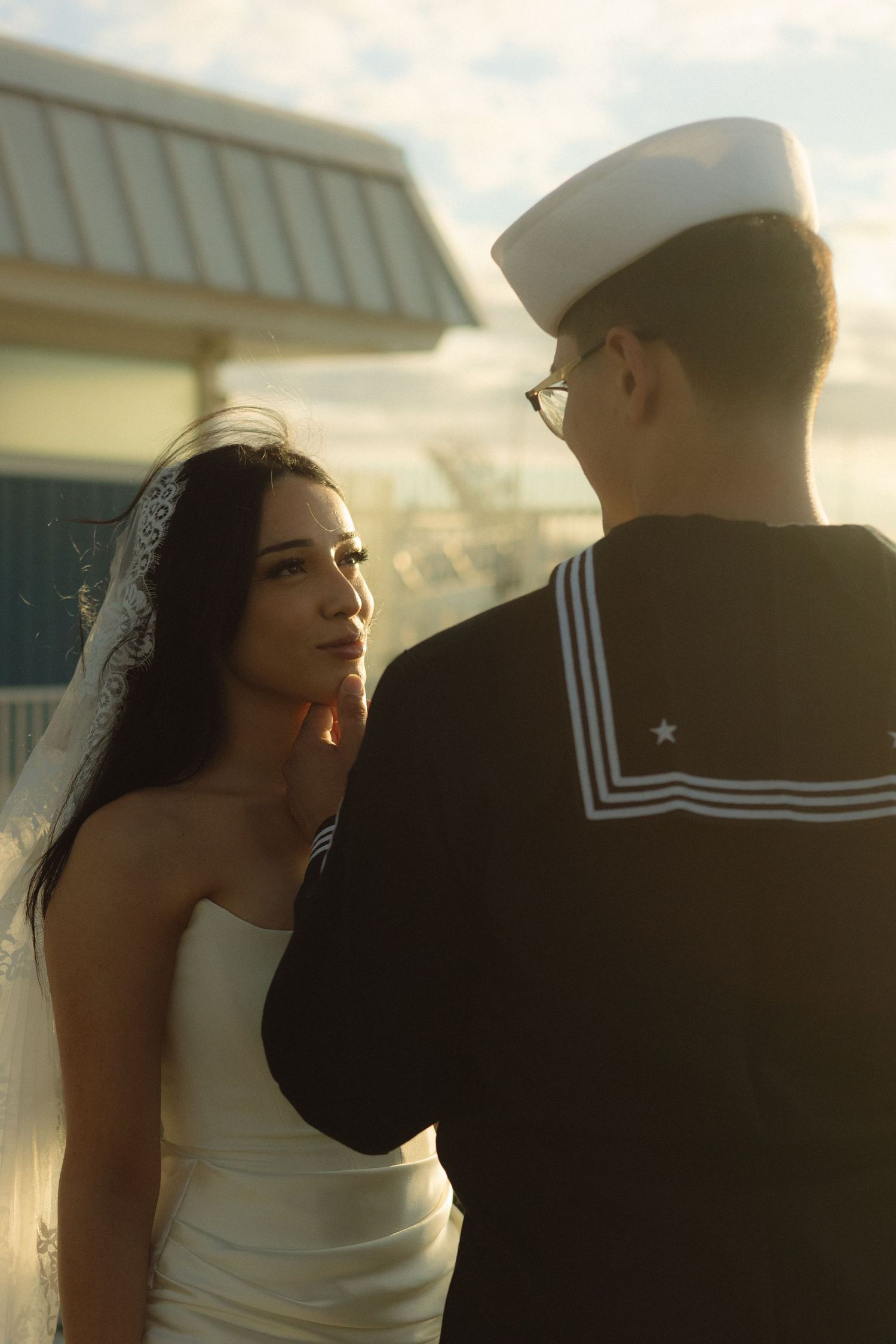 A sailor and bride share an intimate moment at sunset during their wedding photoshoot.