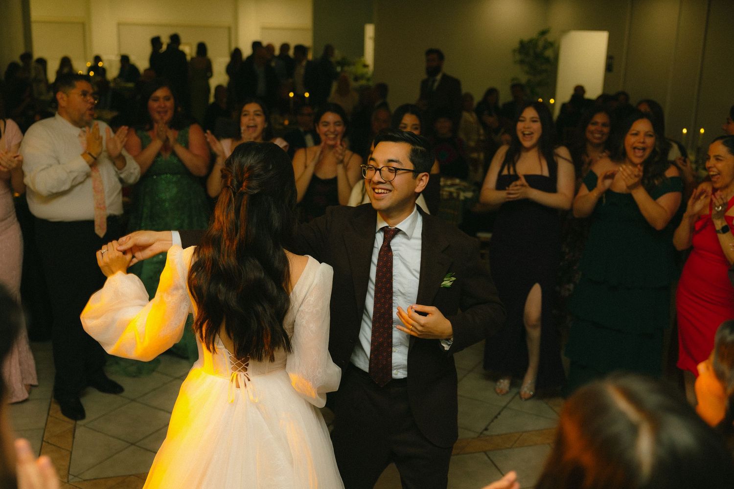 Guests dance and celebrate at an indoor wedding reception with warm lighting and formal attire.