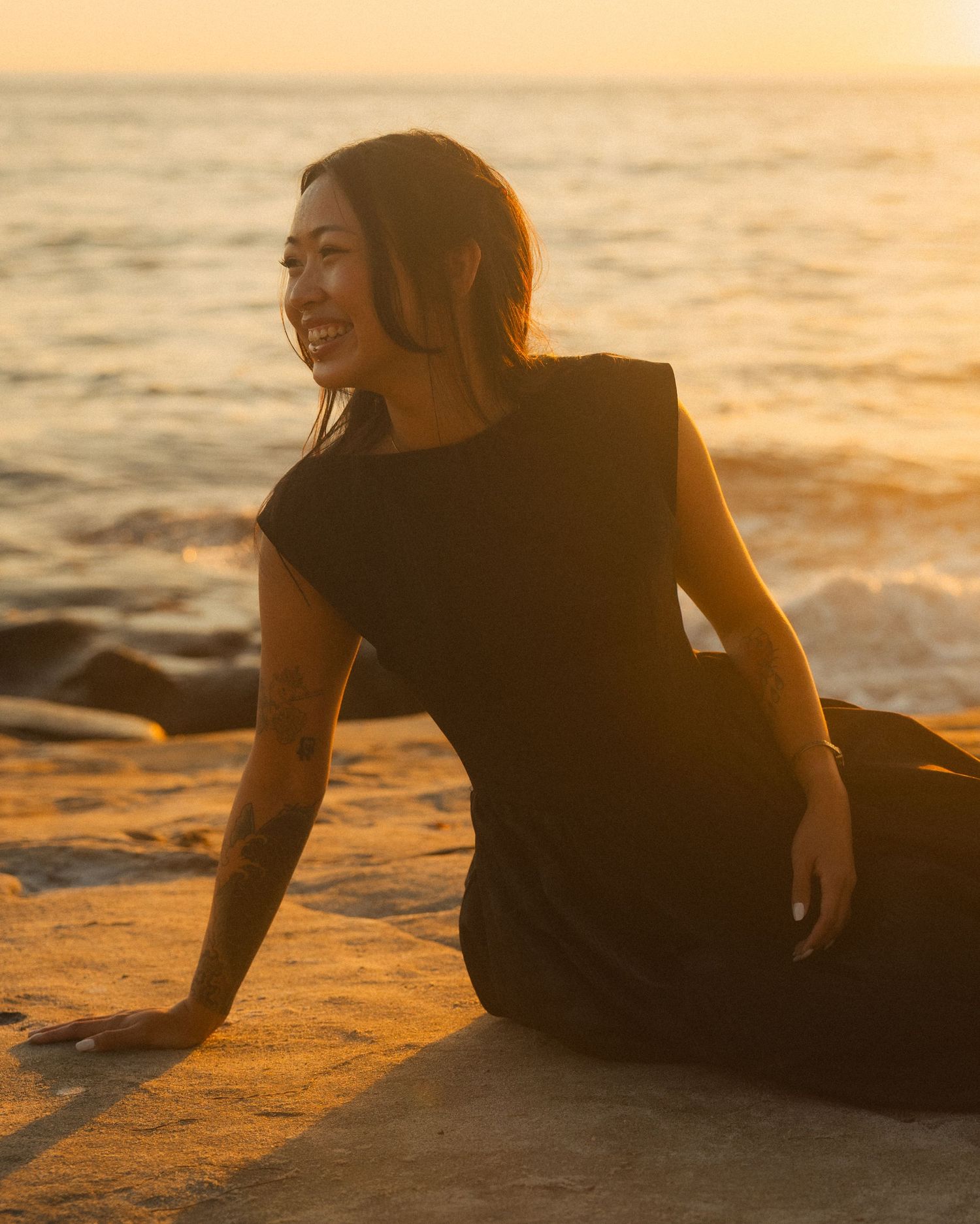 A silhouetted figure relaxes on a sandy beach at sunset with golden light reflecting off the ocean waves.