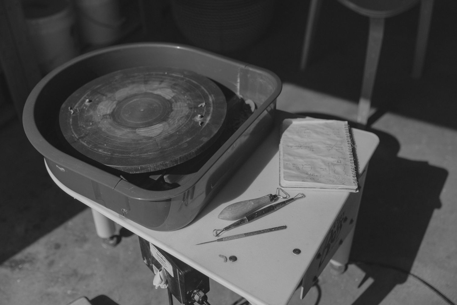 Black and white image of pottery wheel with clay and notepad on surface for a branding session