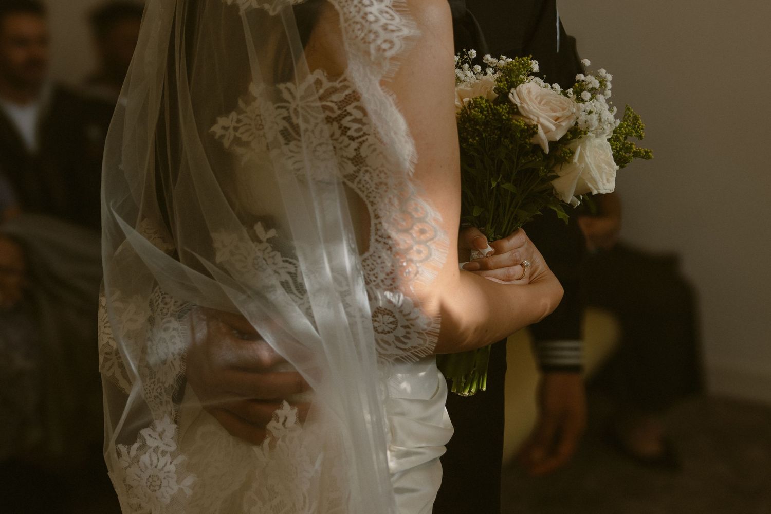 A close-up view of delicate lace details on a white wedding veil and dress in warm, moody lighting.