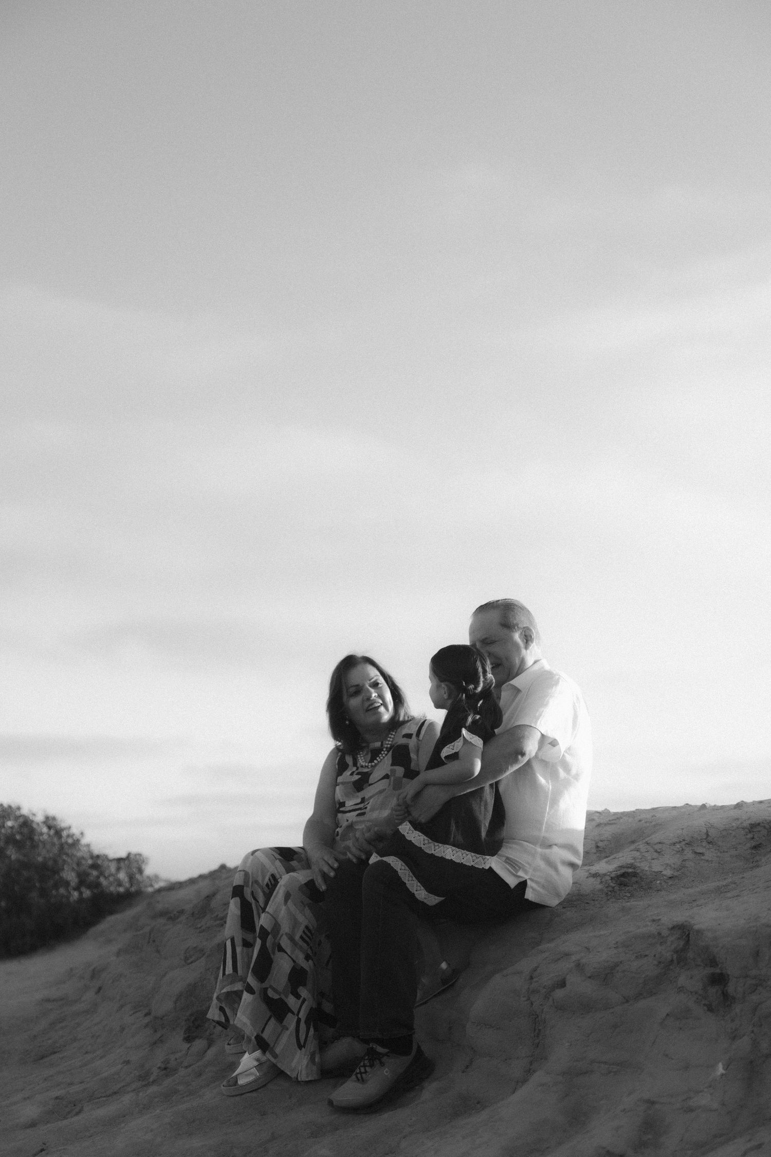 A black and white photograph of a family sitting together on a sandy hill against an overcast sky.
