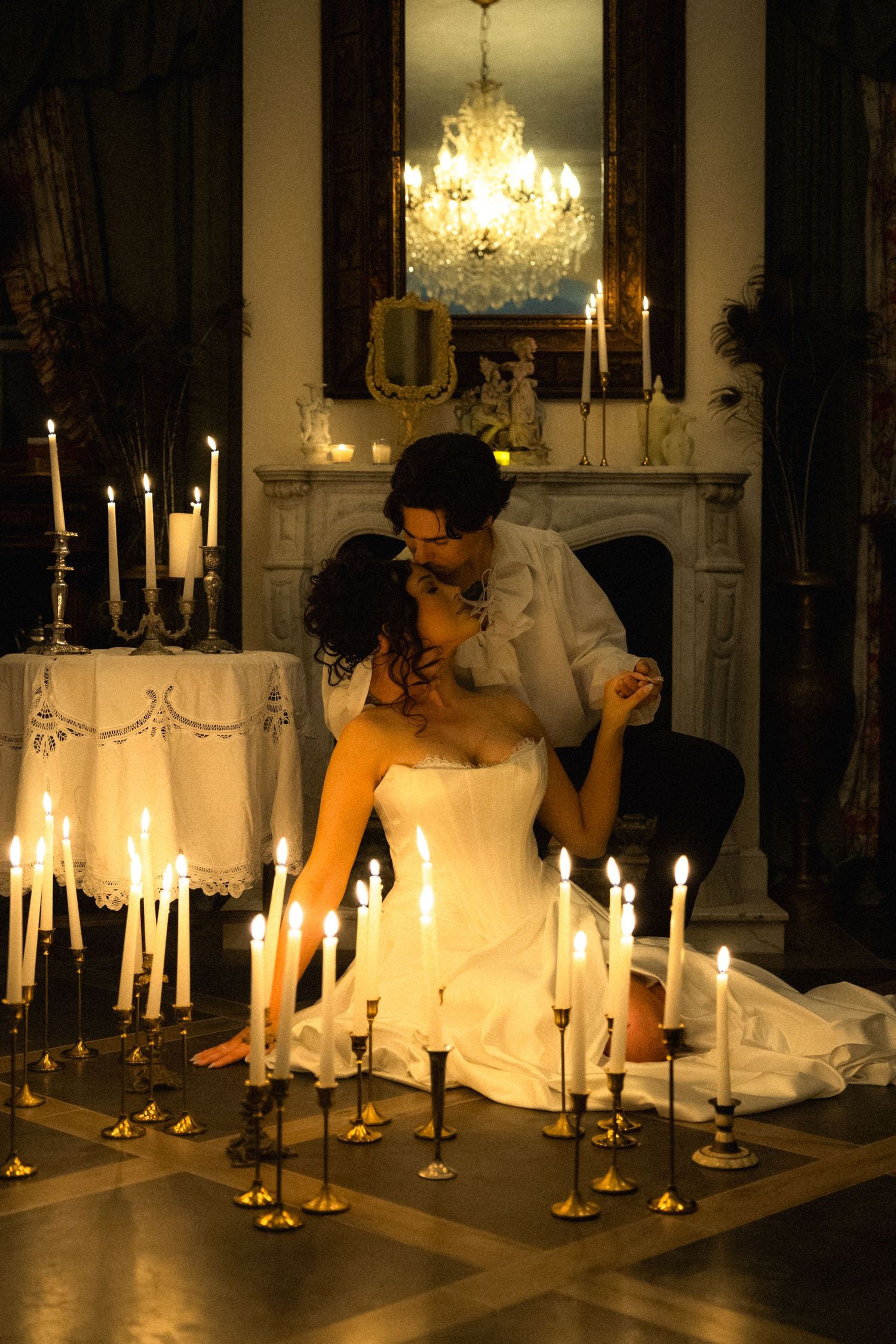 Elegant scene with white-dressed figure among many lit candles beneath a crystal chandelier.