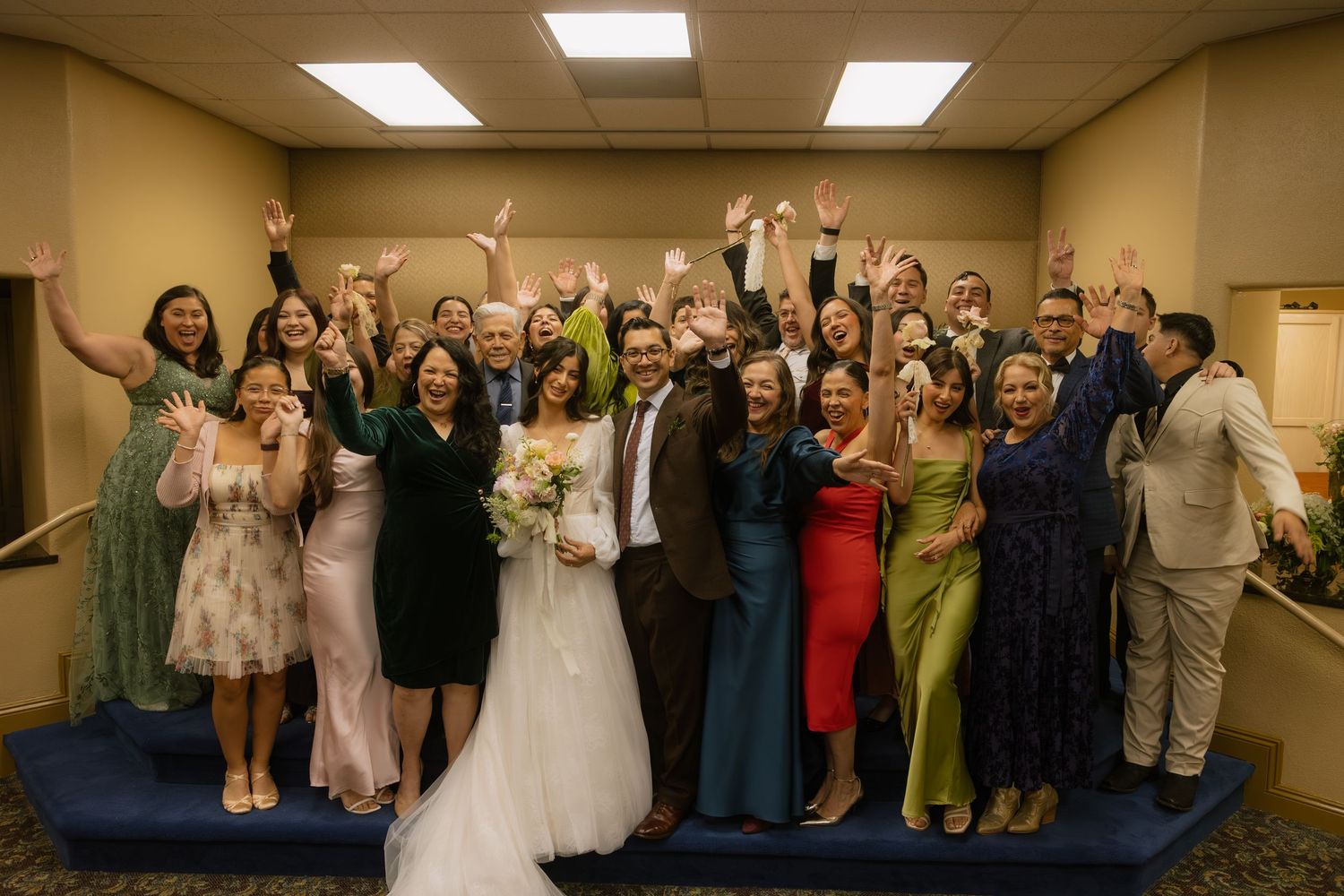 Wedding guests pose together in a brightly lit room during celebration festivities.