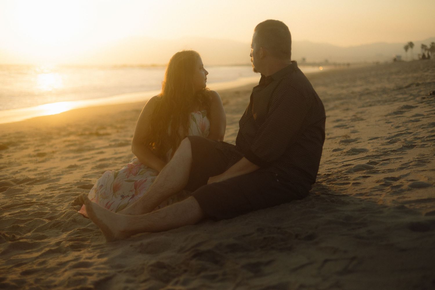 Silhouette of a couple sitting close together on a beach at golden hour sunset.