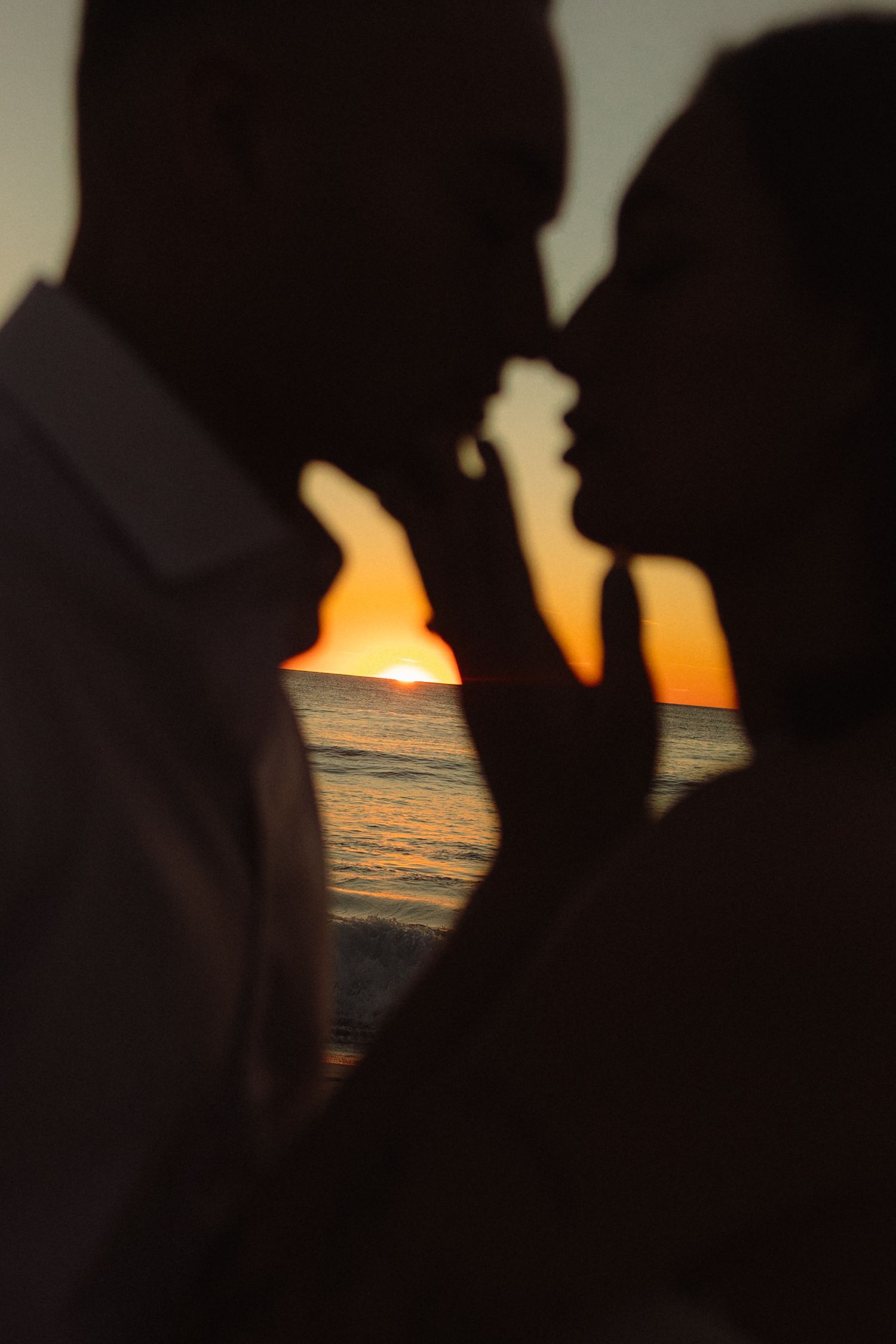 Silhouetted figures stand against a dramatic orange and purple sunset over the ocean horizon.