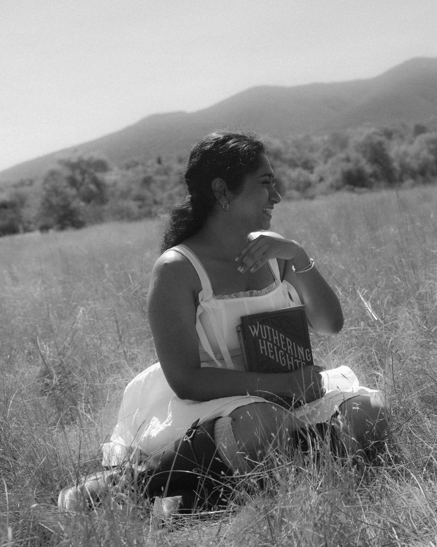 Two people lying in a grassy field reading books together in black and white.