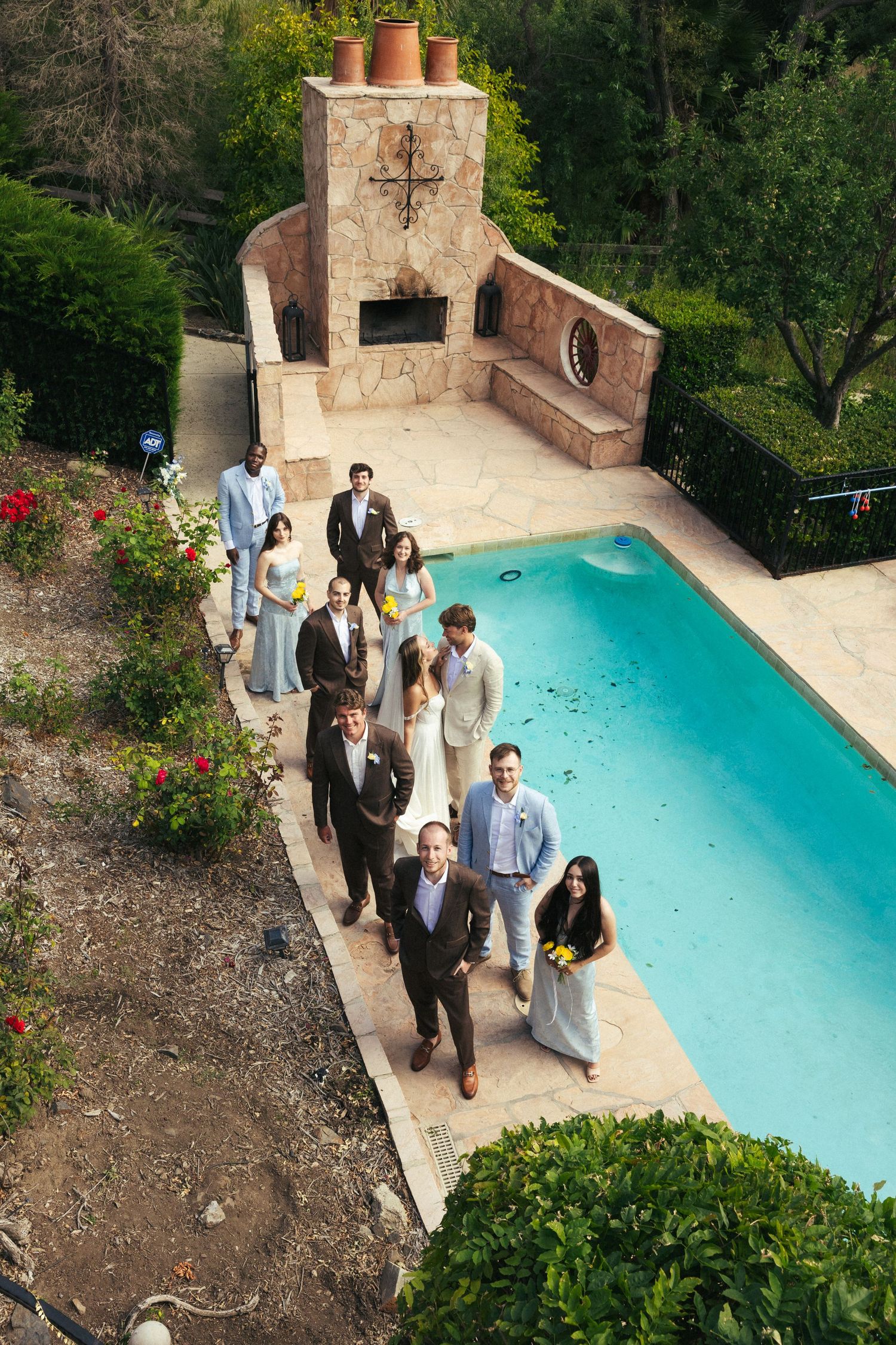 Wedding party walking poolside near stone fireplace outdoor venue aerial view.
