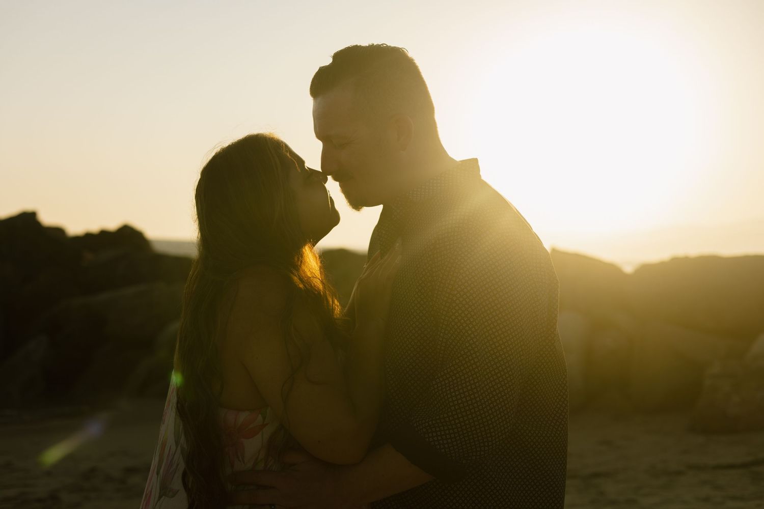 Silhouetted couple lean in close at sunset with golden sun rays creating a romantic backlit glow.