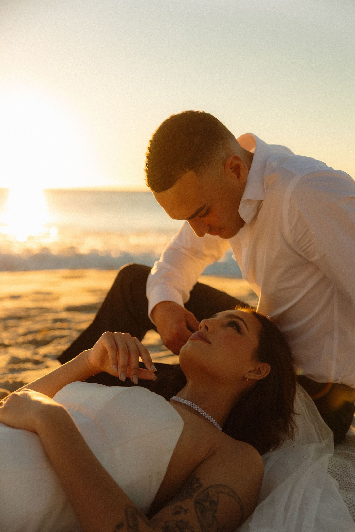 A romantic couple embraces on the beach at sunset with golden light illuminating their silhouettes.