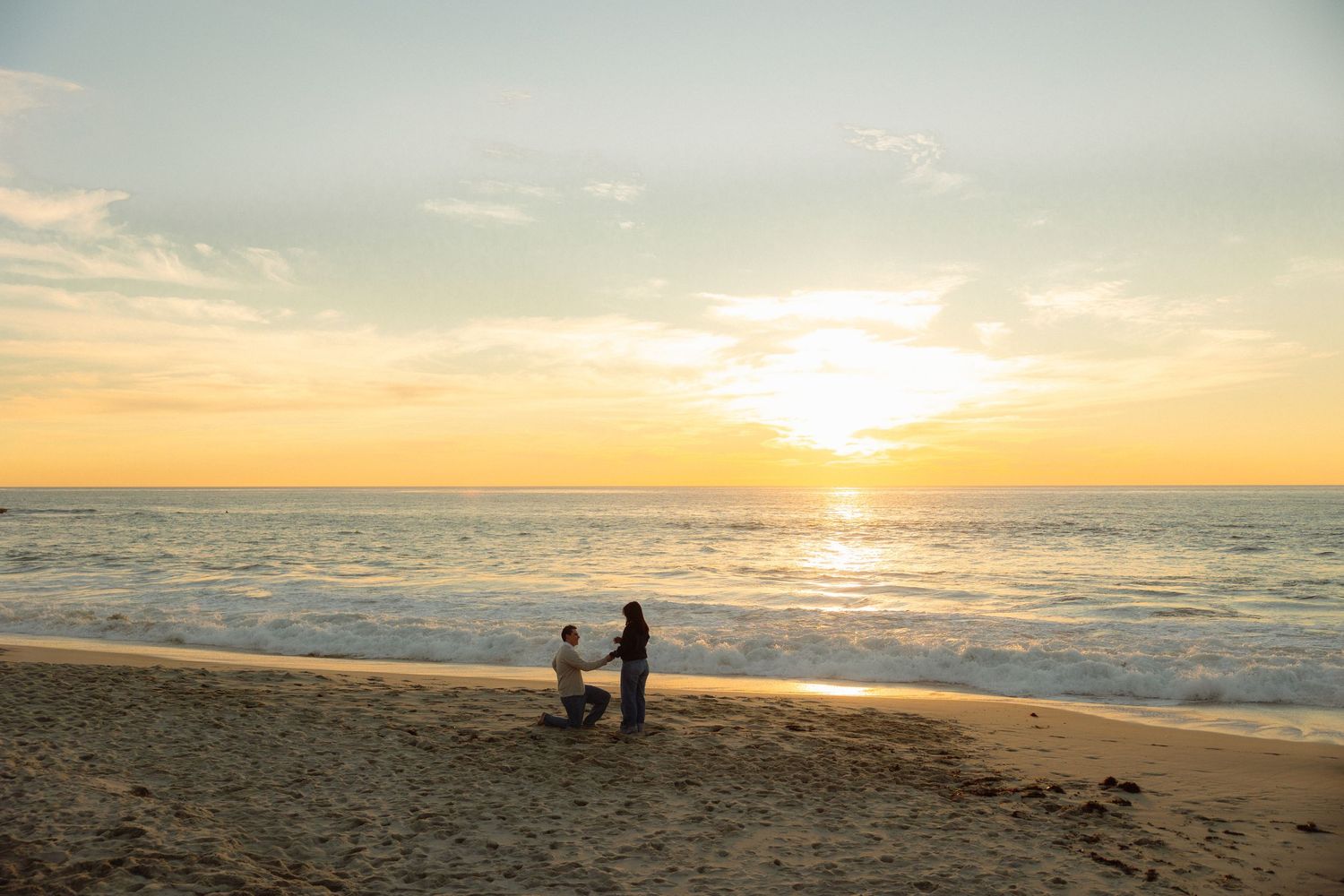 A tranquil beach scene at sunset with gentle waves rolling onto shore and silhouettes against the golden horizon.