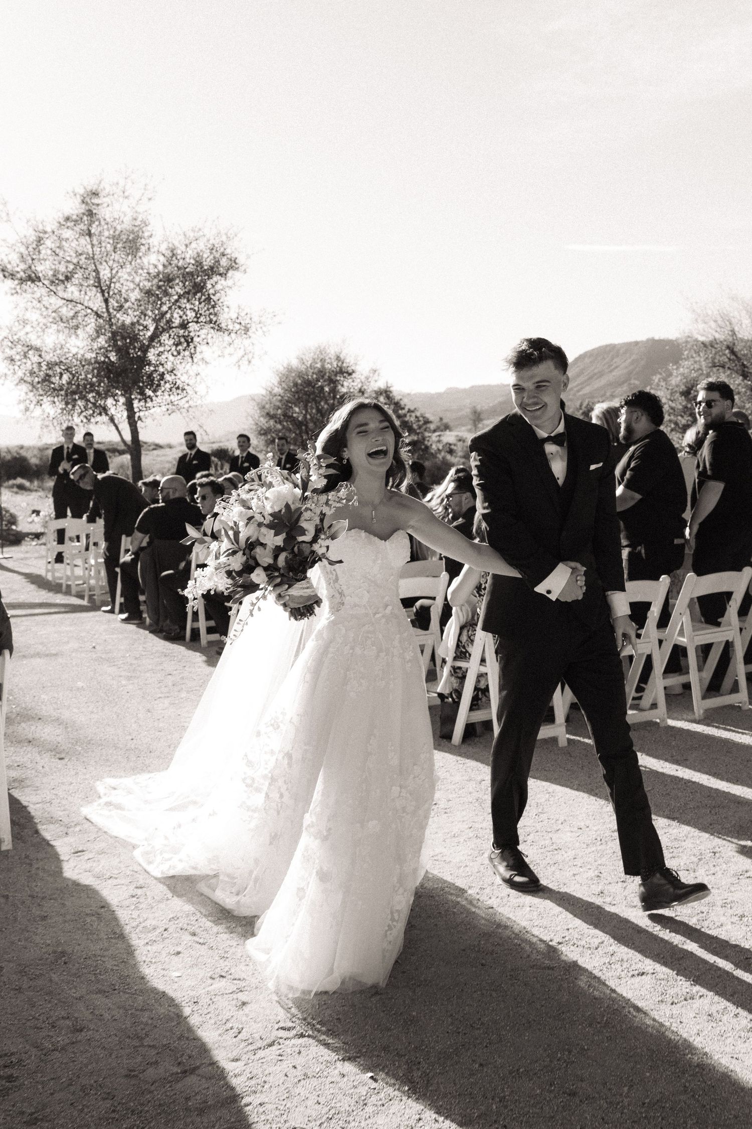 Black and white photo of a joyful bride and groom walking back down the aisle after their outdoor wedding ceremony.