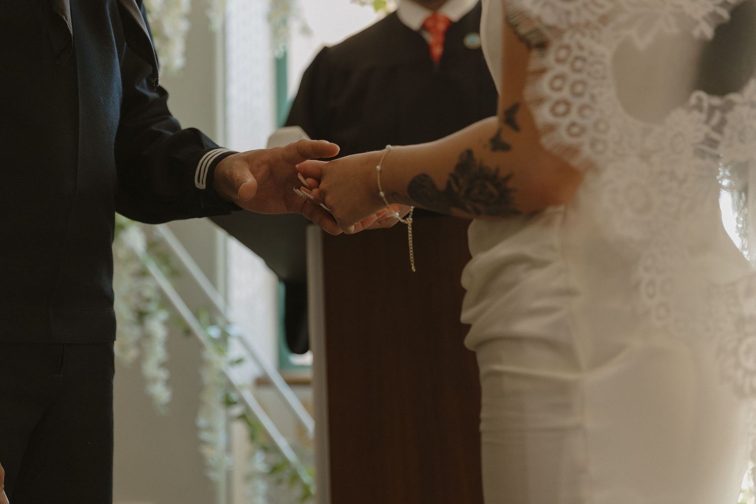 Two people exchange rings during an intimate wedding ceremony in front of an officiant while wearing lace and black attire.