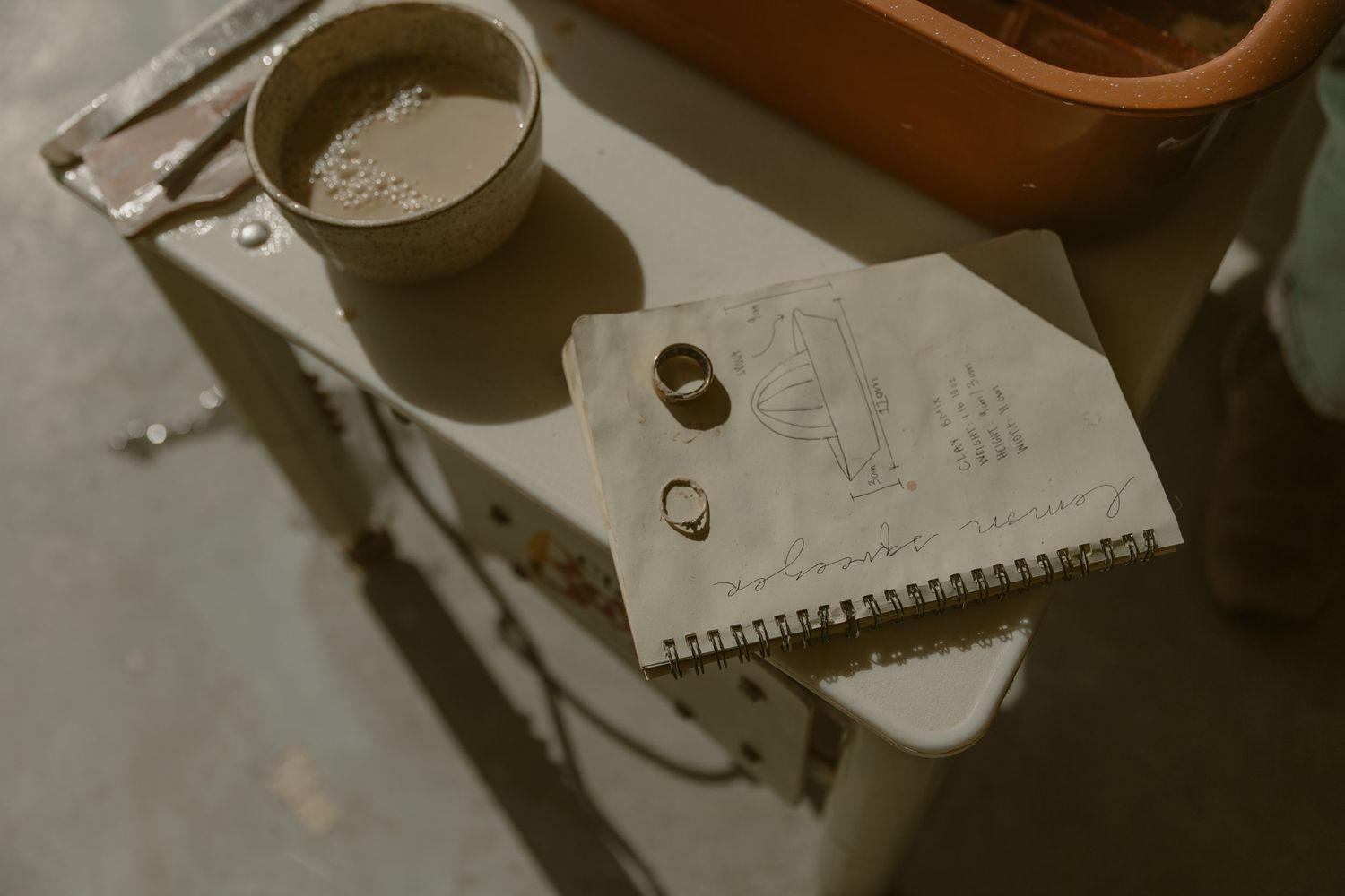 Coffee cup and spiral notebook with rings on a dark surface.