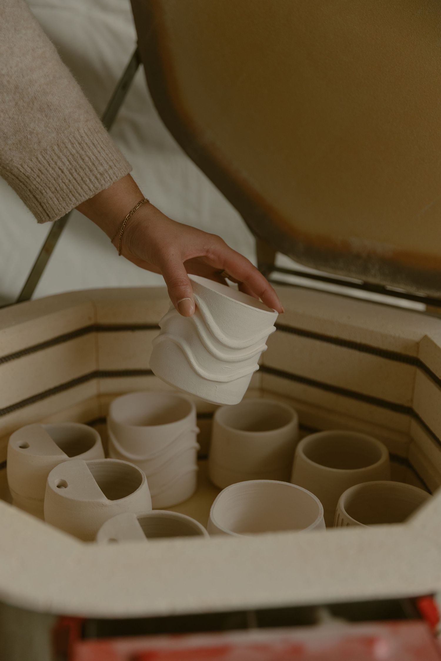 Hand reaching for white ceramic vessels arranged in organized rows for a ceramics branding session