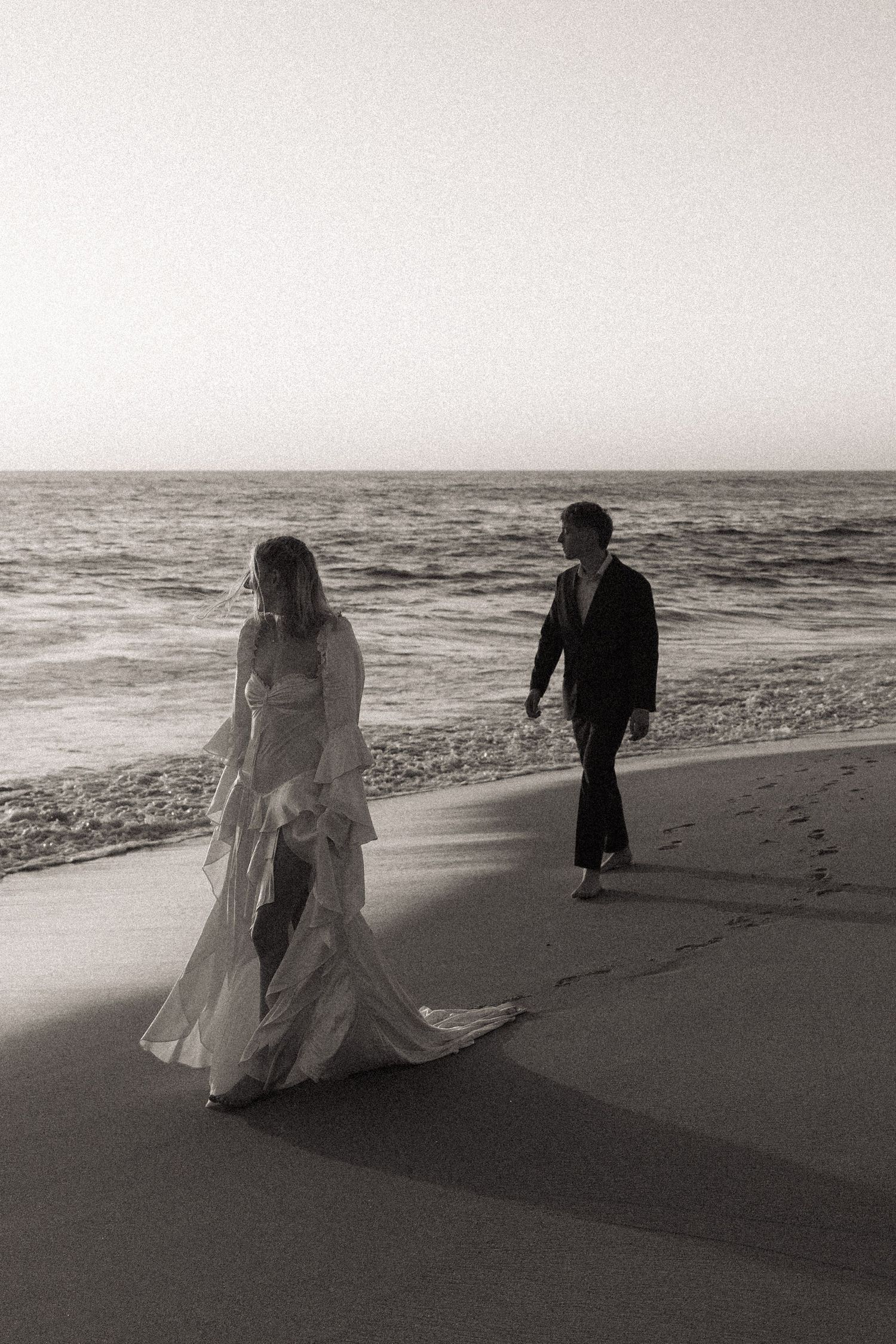 A couple takes romantic black and white photos along a misty beach shoreline.