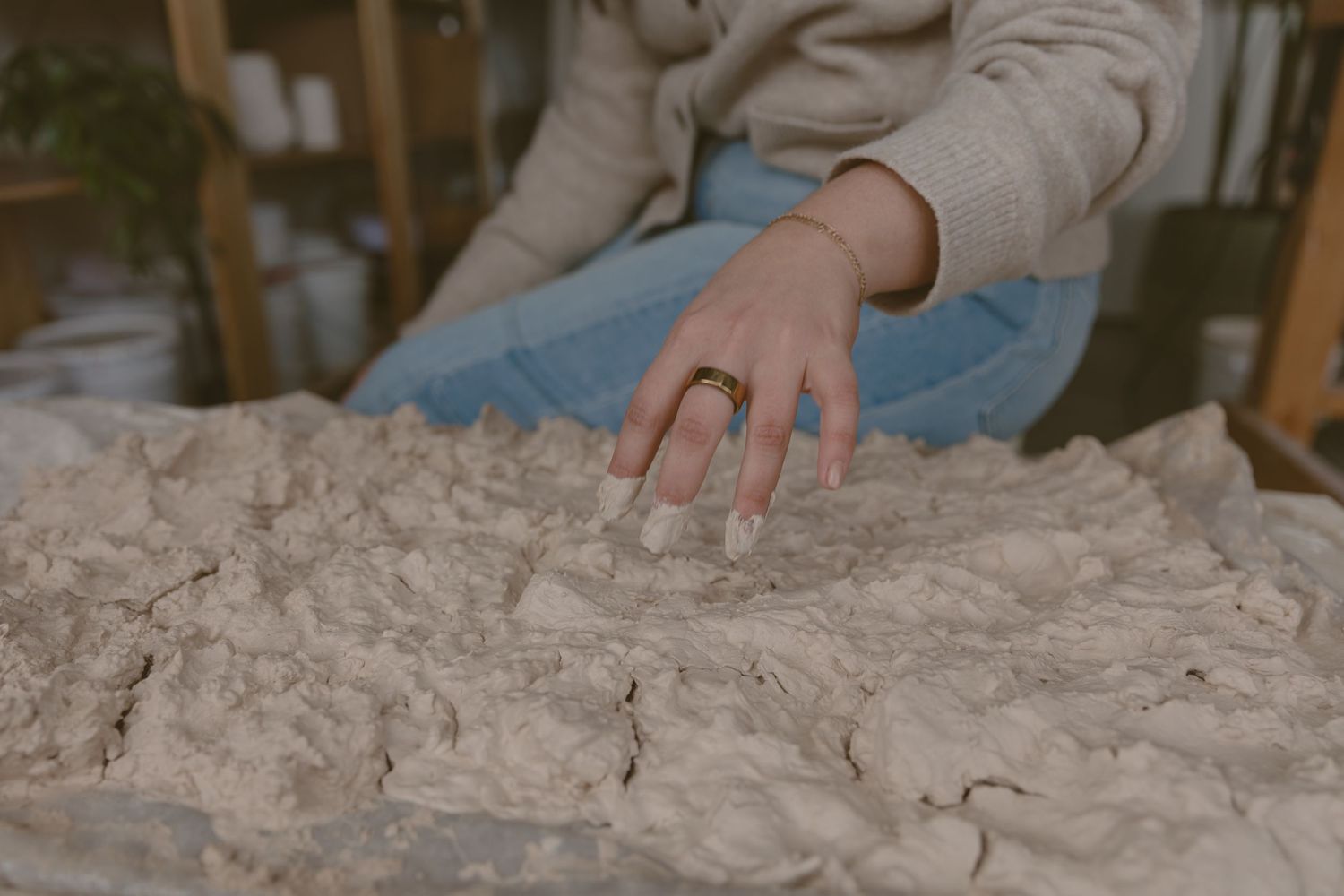 Hand touching raw clay texture in a pottery studio.