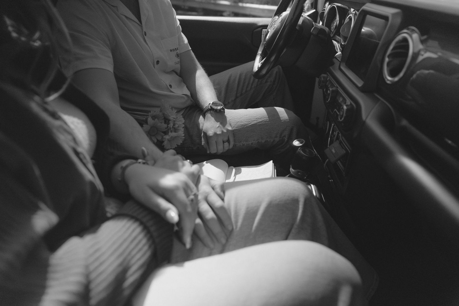 Intimate black and white photo of hands clasped together in a car interior.